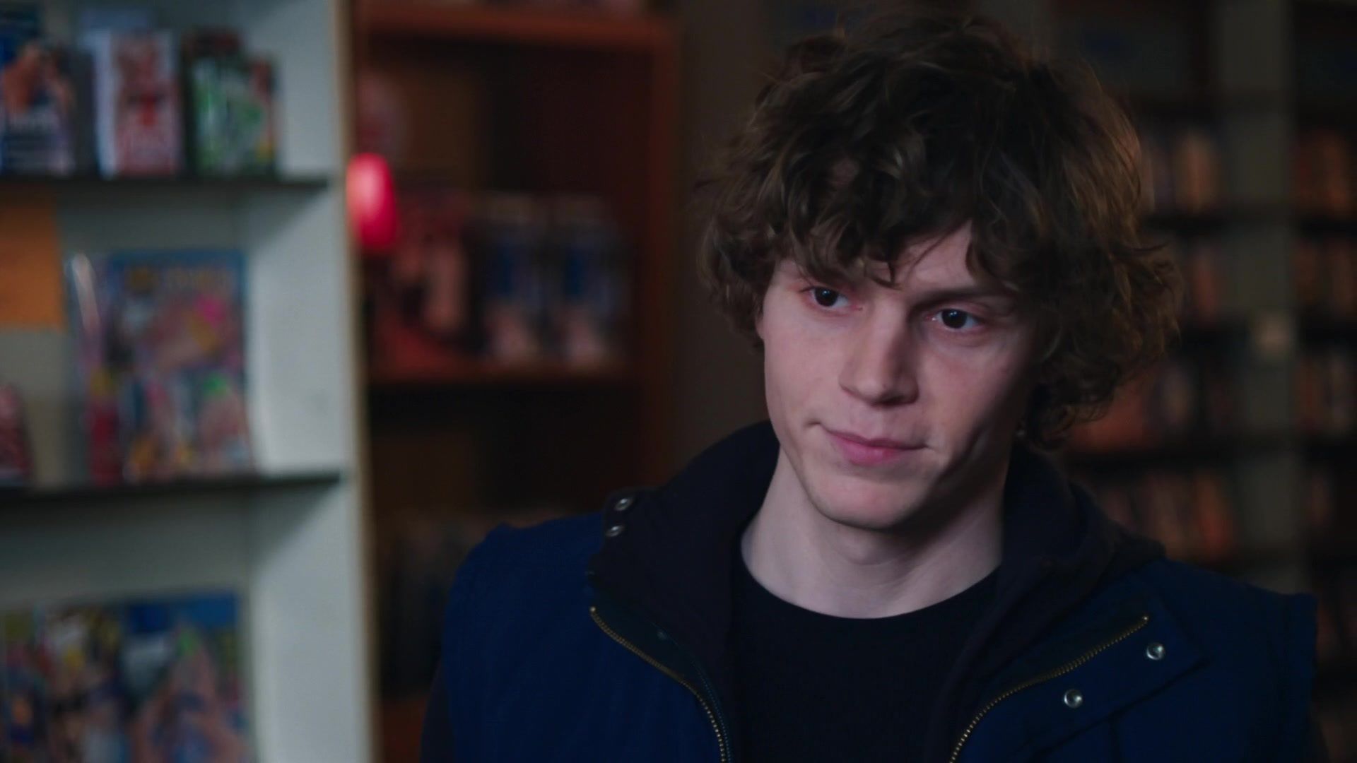 A young man with curly hair in front of books - Evan Peters