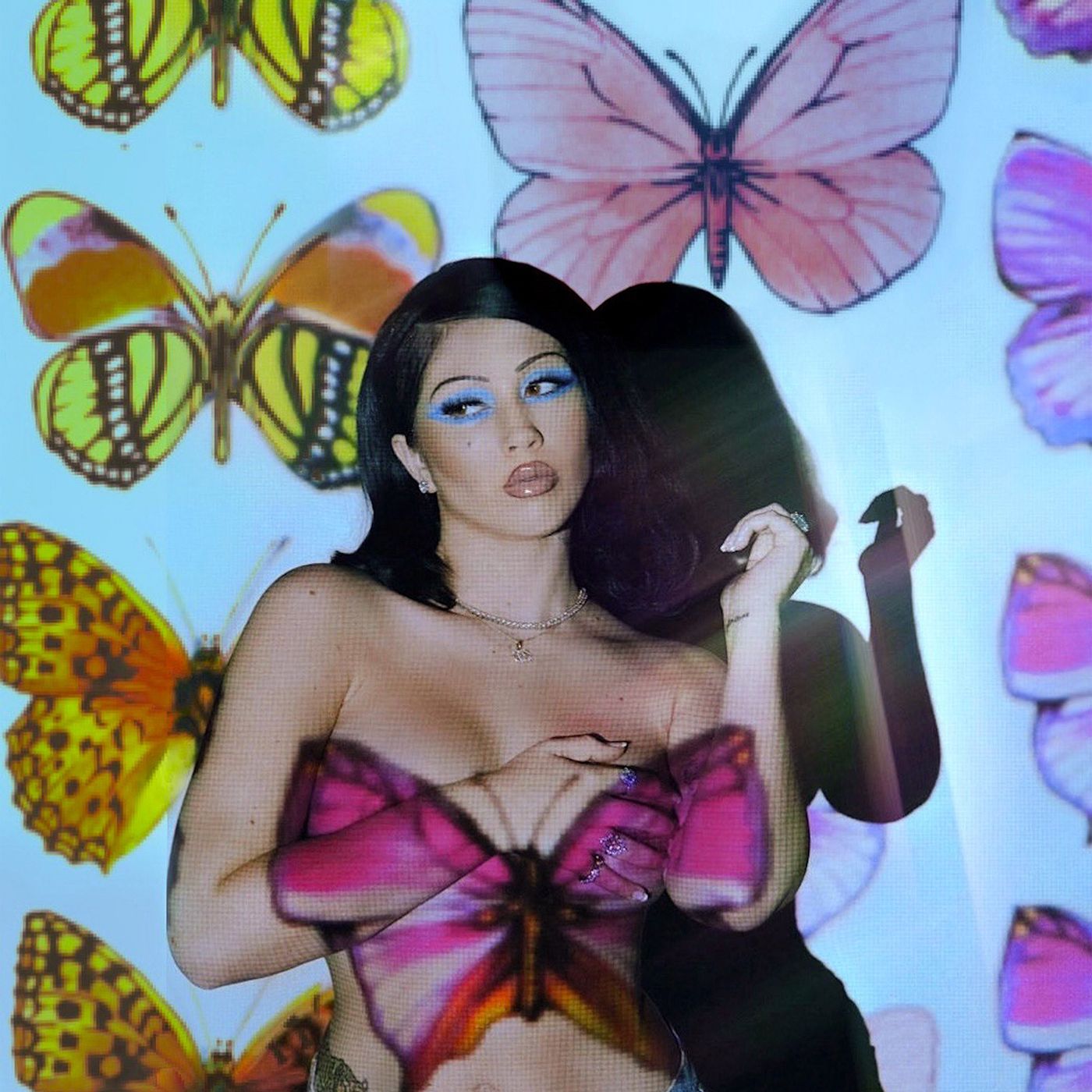 A woman with a butterfly-themed top and butterfly wallpaper behind her - Kali Uchis