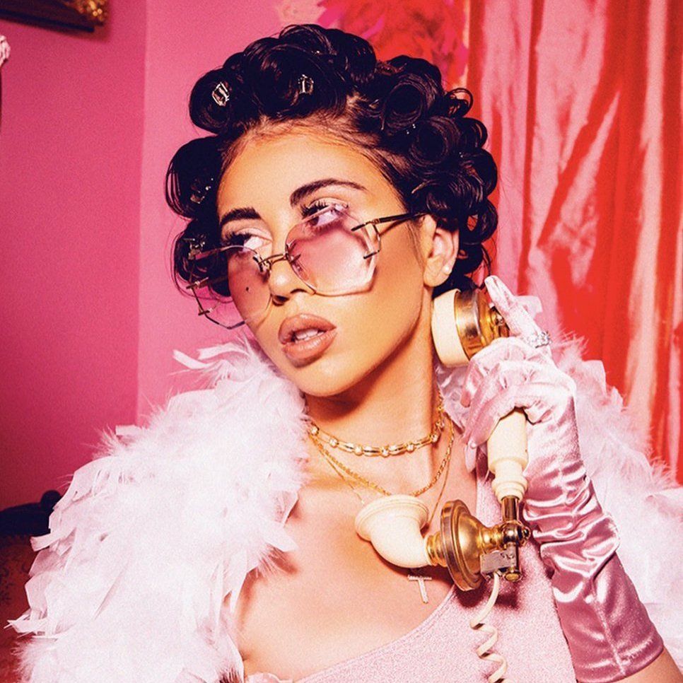 A woman with a pink background wearing a pink top and a pink boa - Kali Uchis