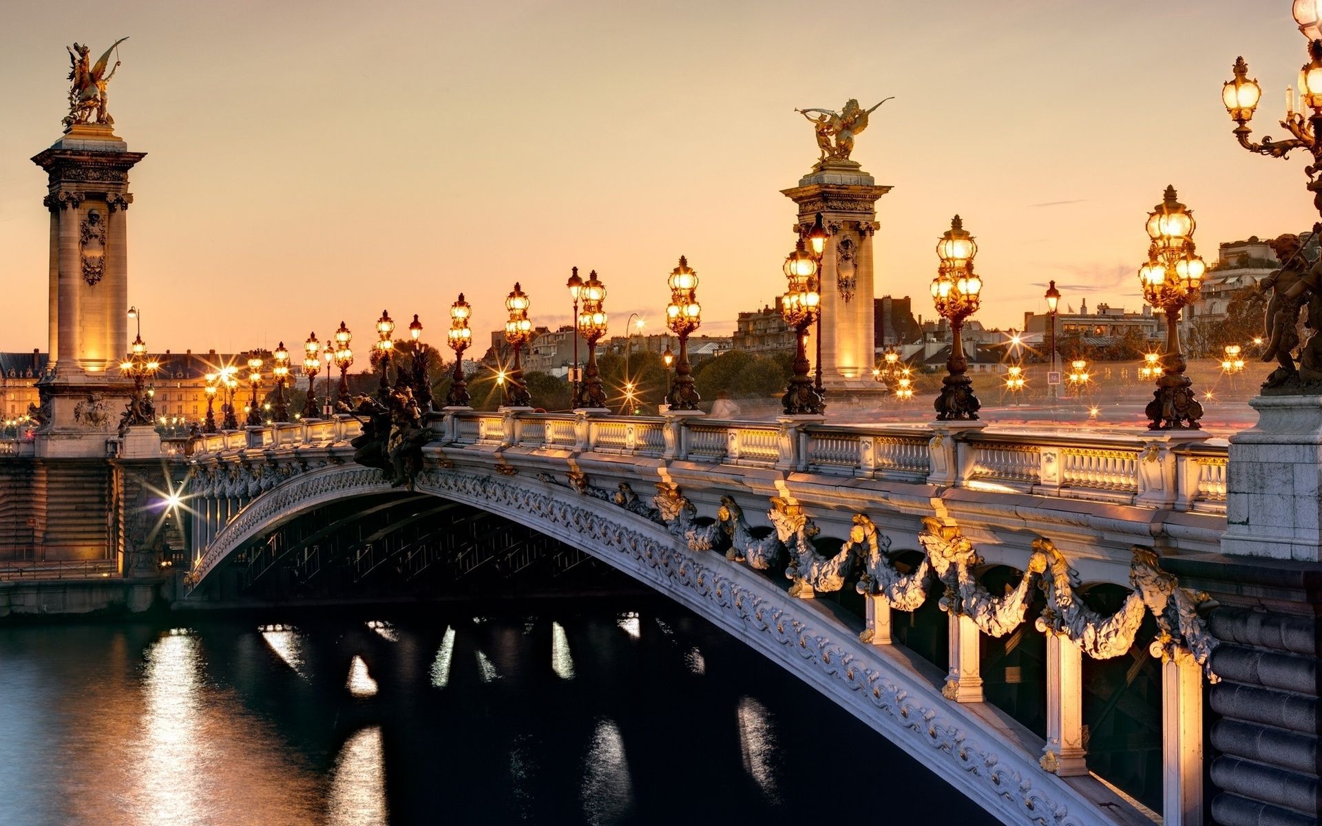 A bridge in Paris at sunset with street lights illuminating the scene. - Paris