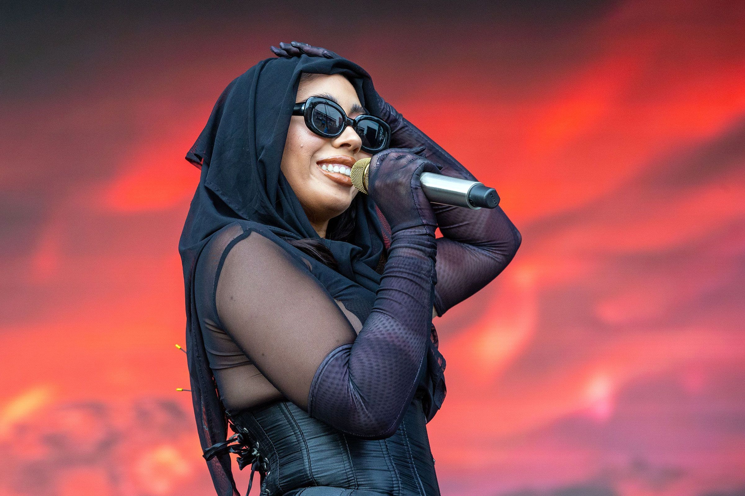 Azealia Banks in a black outfit and sunglasses singing into a microphone - Kali Uchis