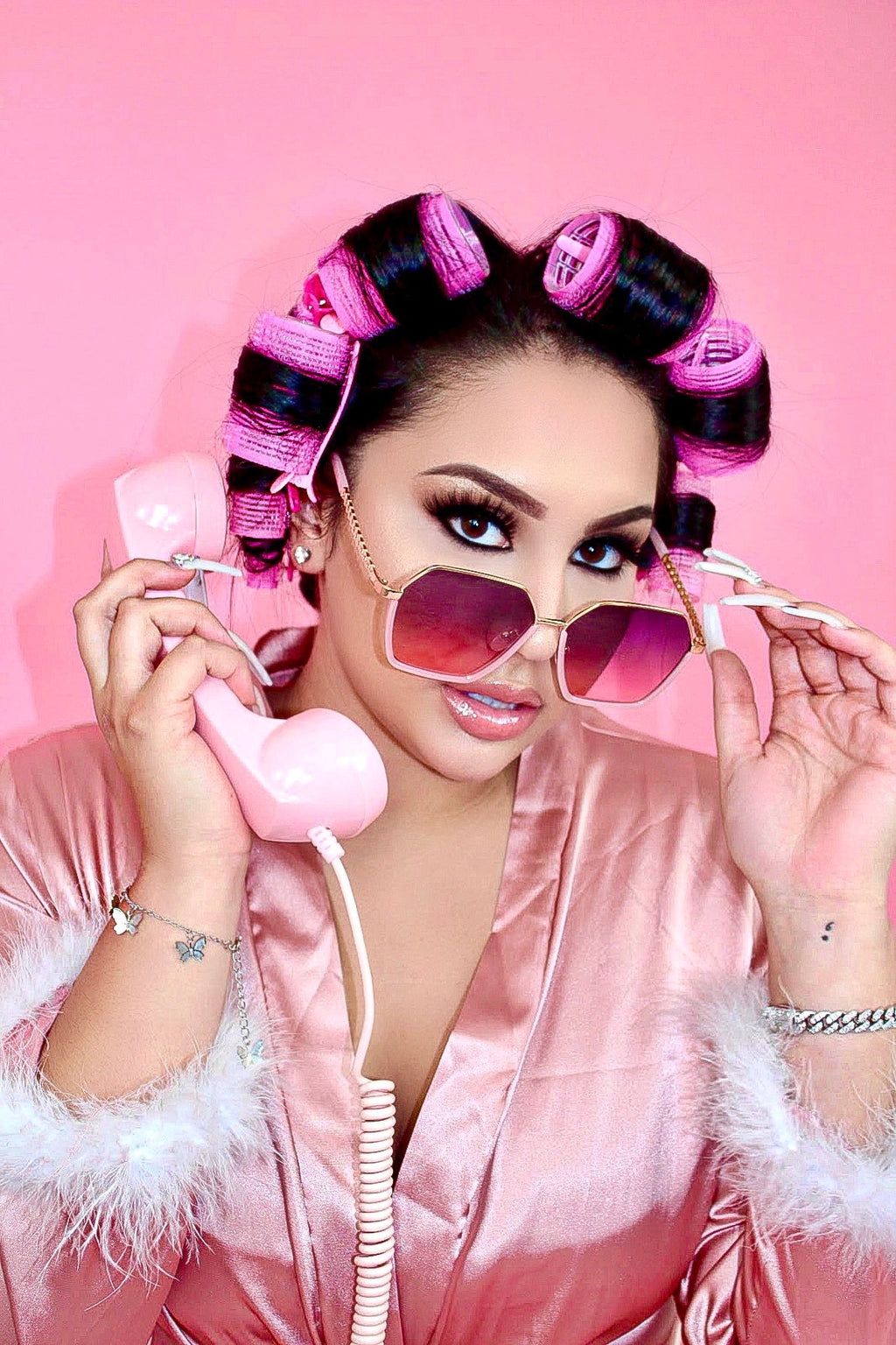 A woman in pink robe and sunglasses holding up phone - Kali Uchis