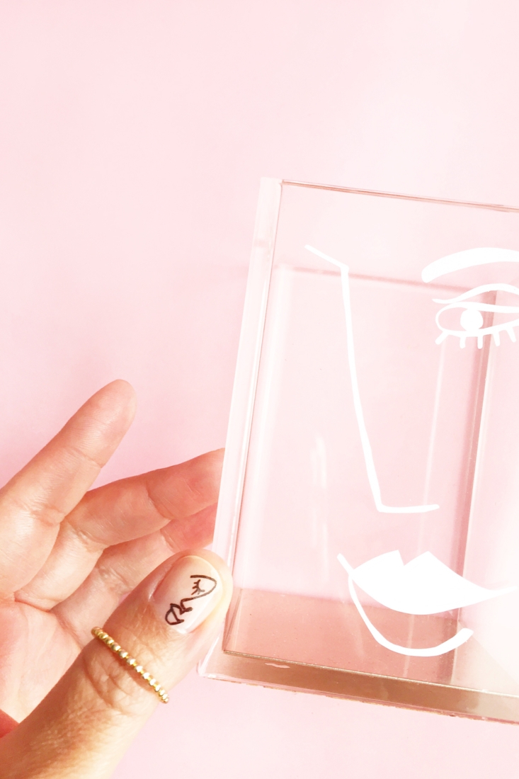 A hand holding a clear glass vase with a face drawn on it - Nails