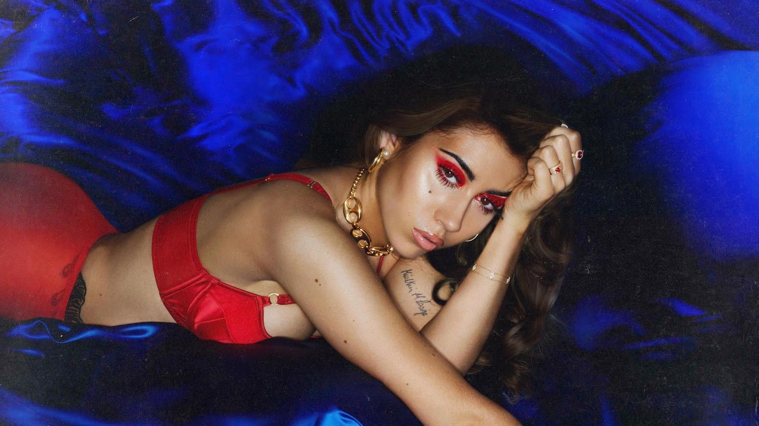 A woman in red lingerie laying on blue bedding - Kali Uchis