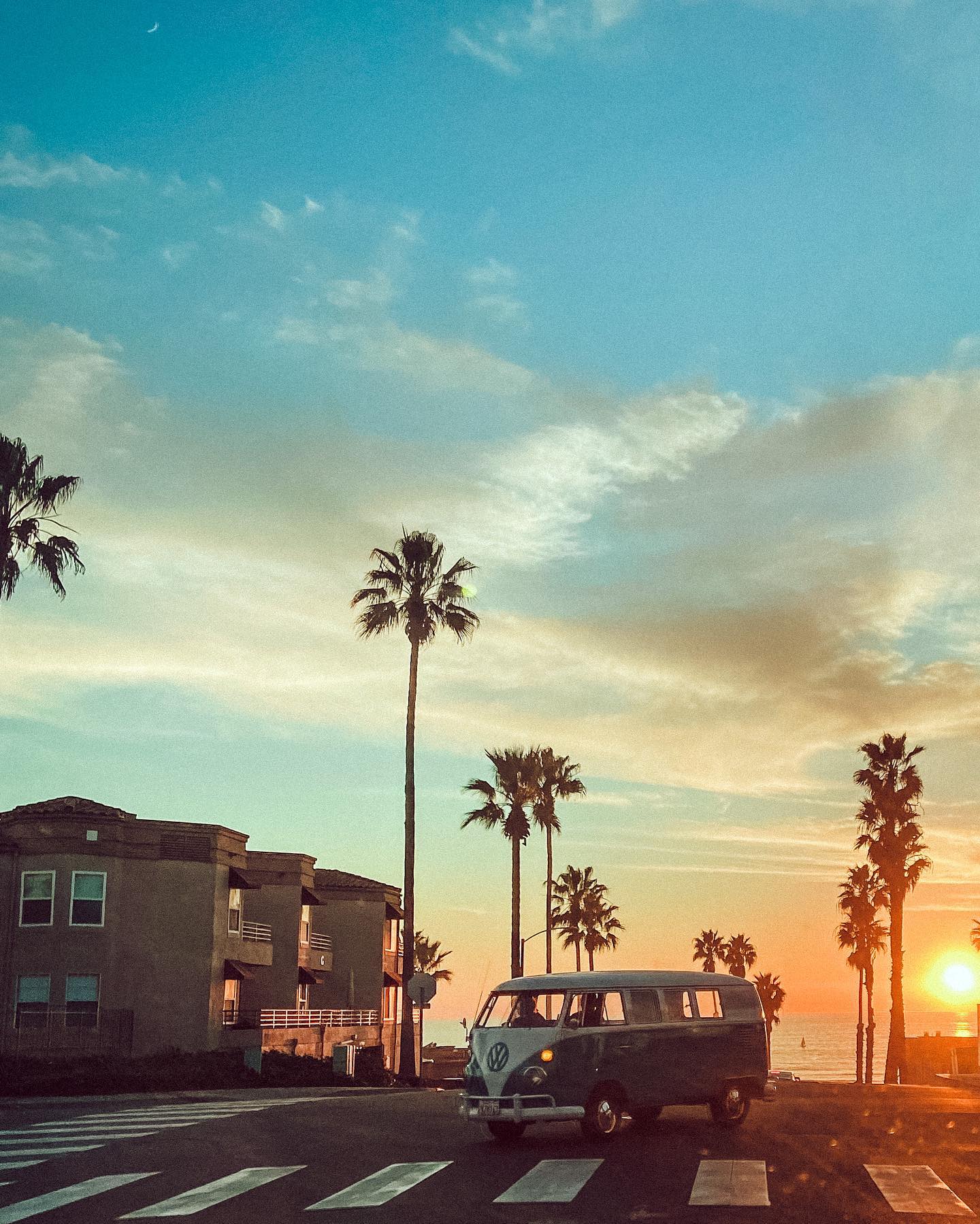 A VW bus parked on the beach with the sunset in the background - California