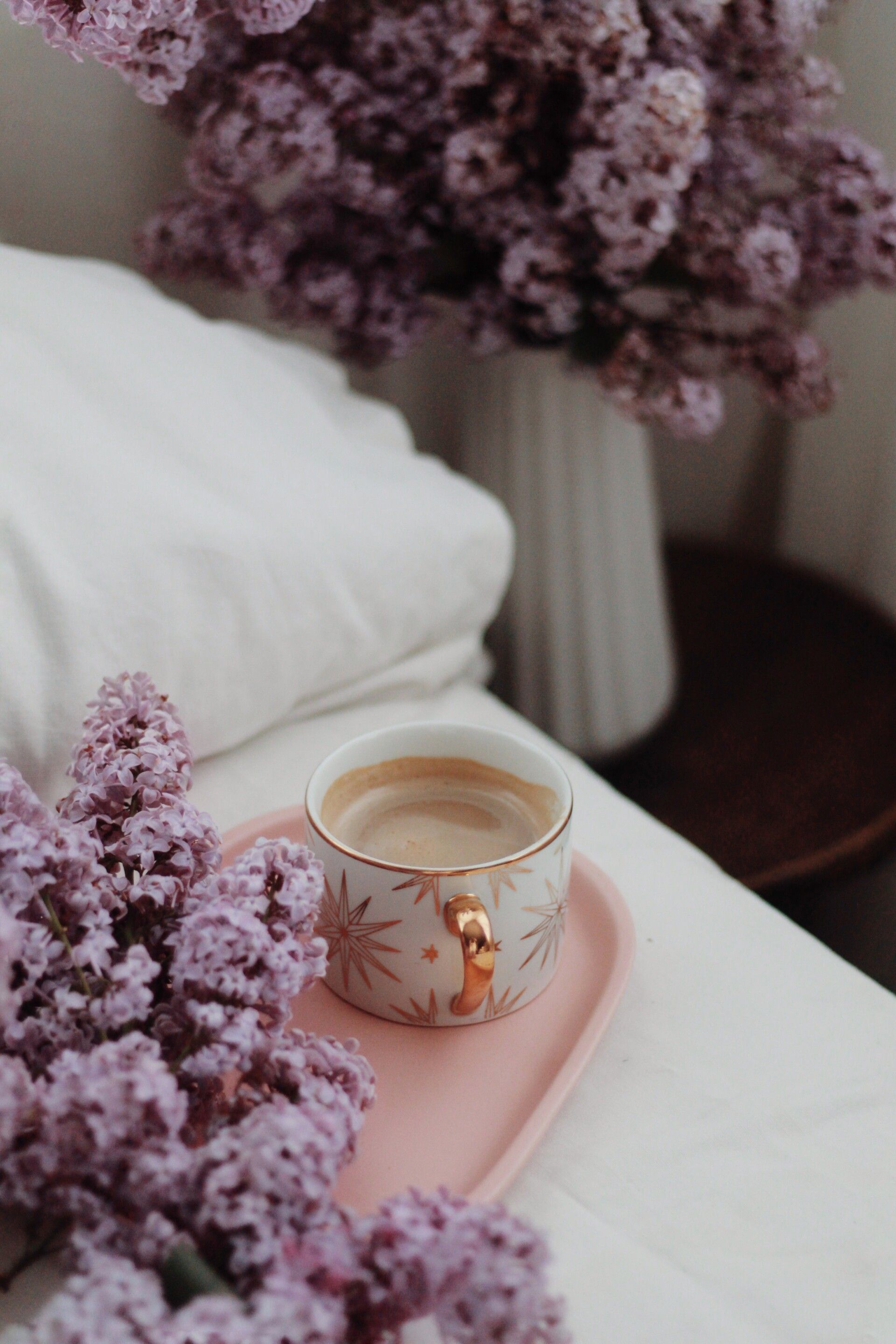 A cup of coffee on a pink tray next to a bunch of purple flowers - Spring