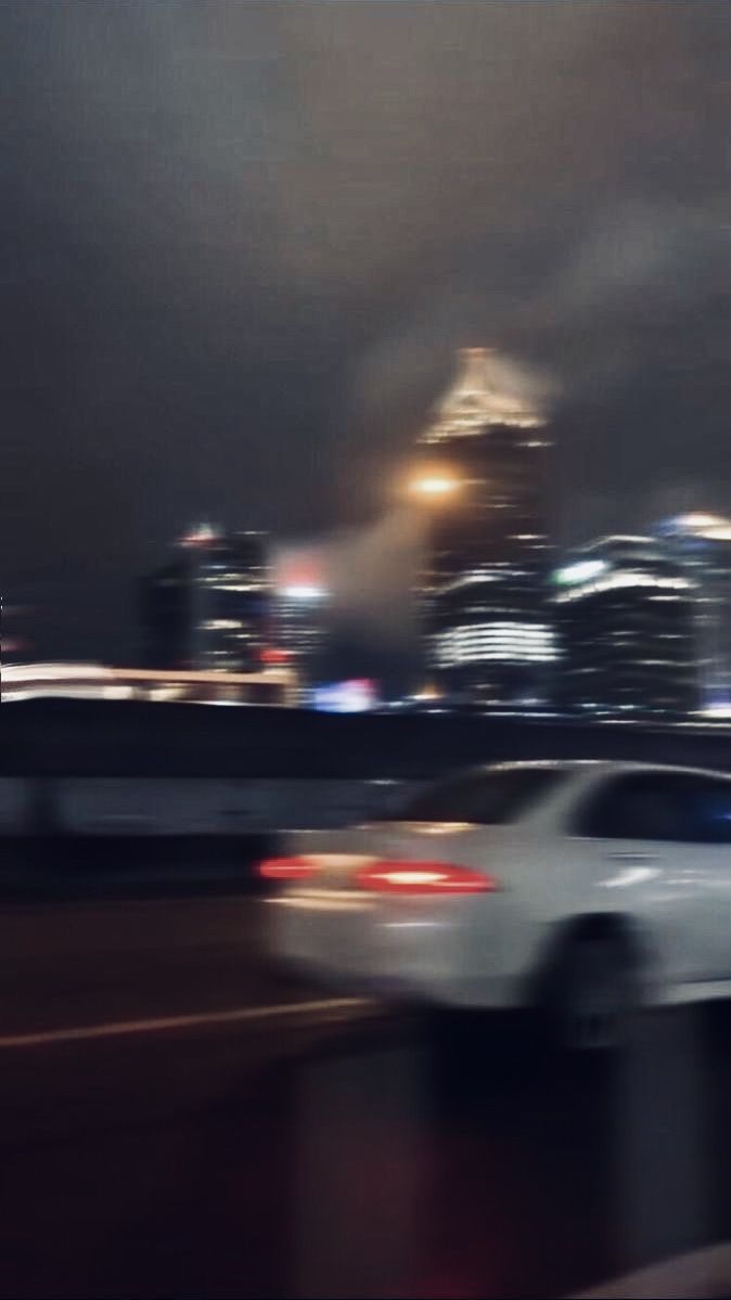 A blurry car driving on a road with a city skyline in the background. - Blurry