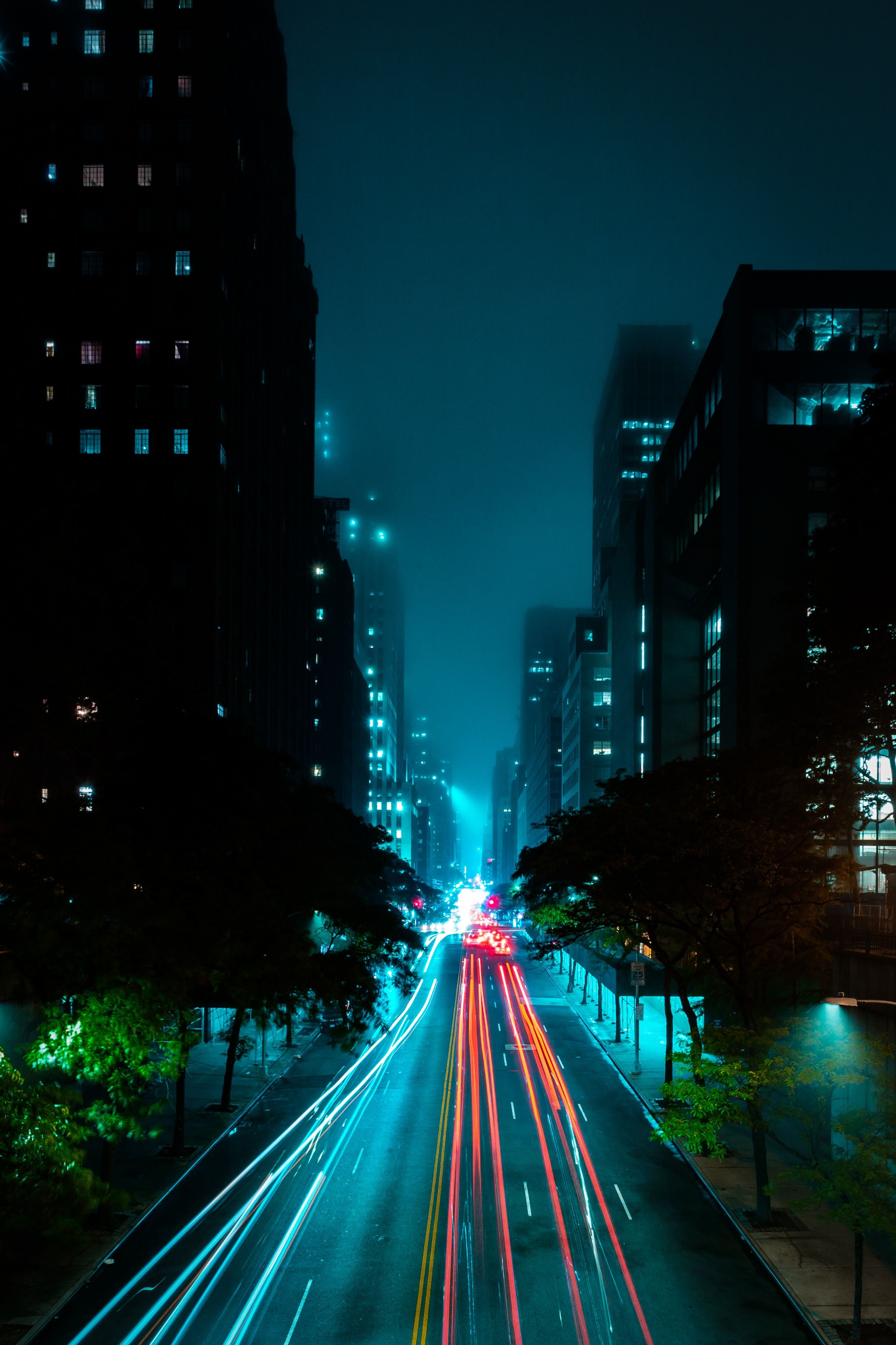 A city street at night with traffic lights and tall buildings. - Night, fog