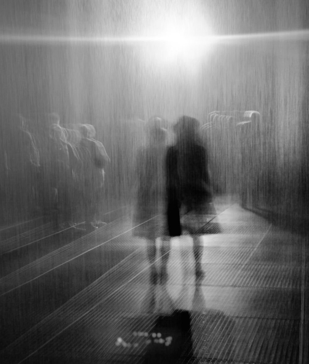 A black and white photo of a person walking in the rain. - Blurry