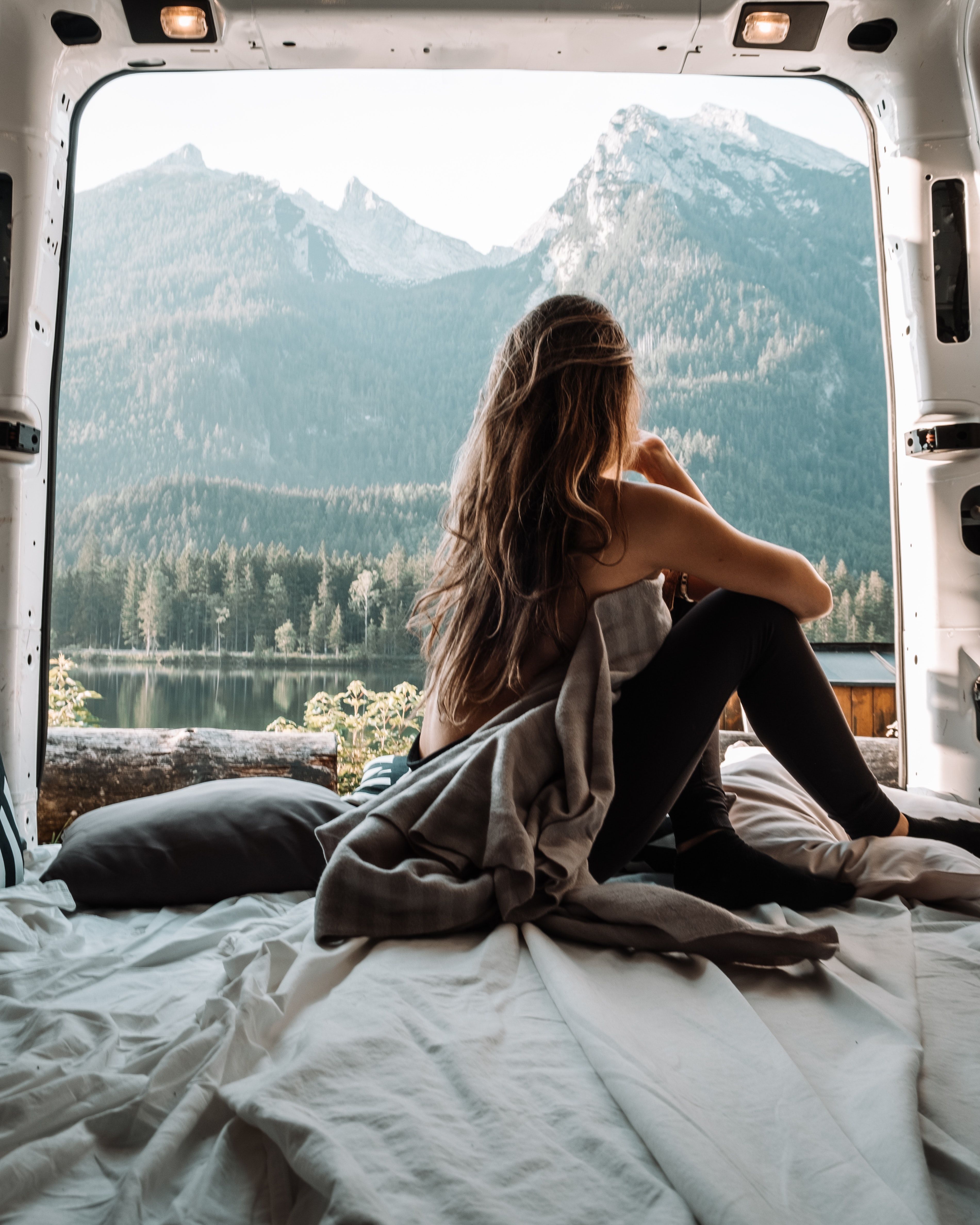 A woman sits on the bed of a van looking out at a mountain. - Travel