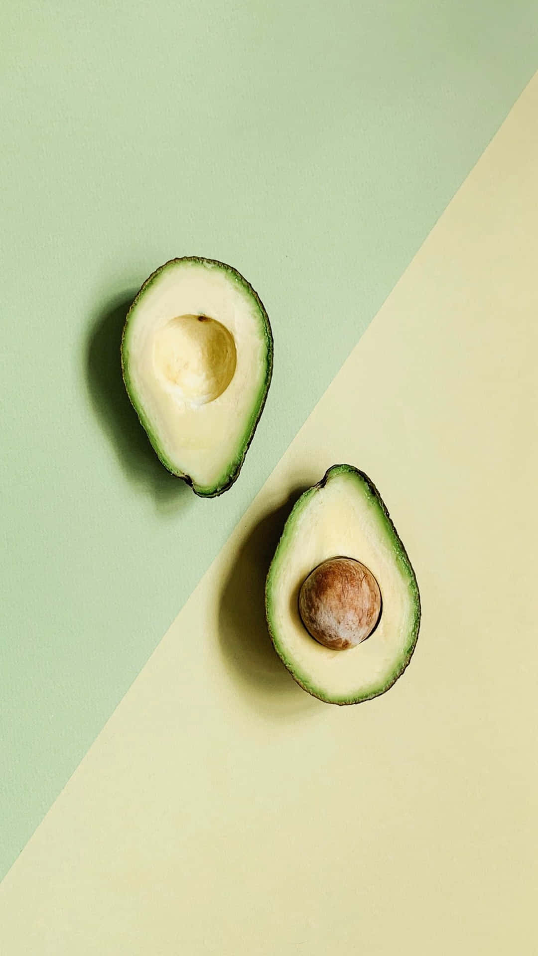 An avocado cut in half on a green and yellow background - Avocado