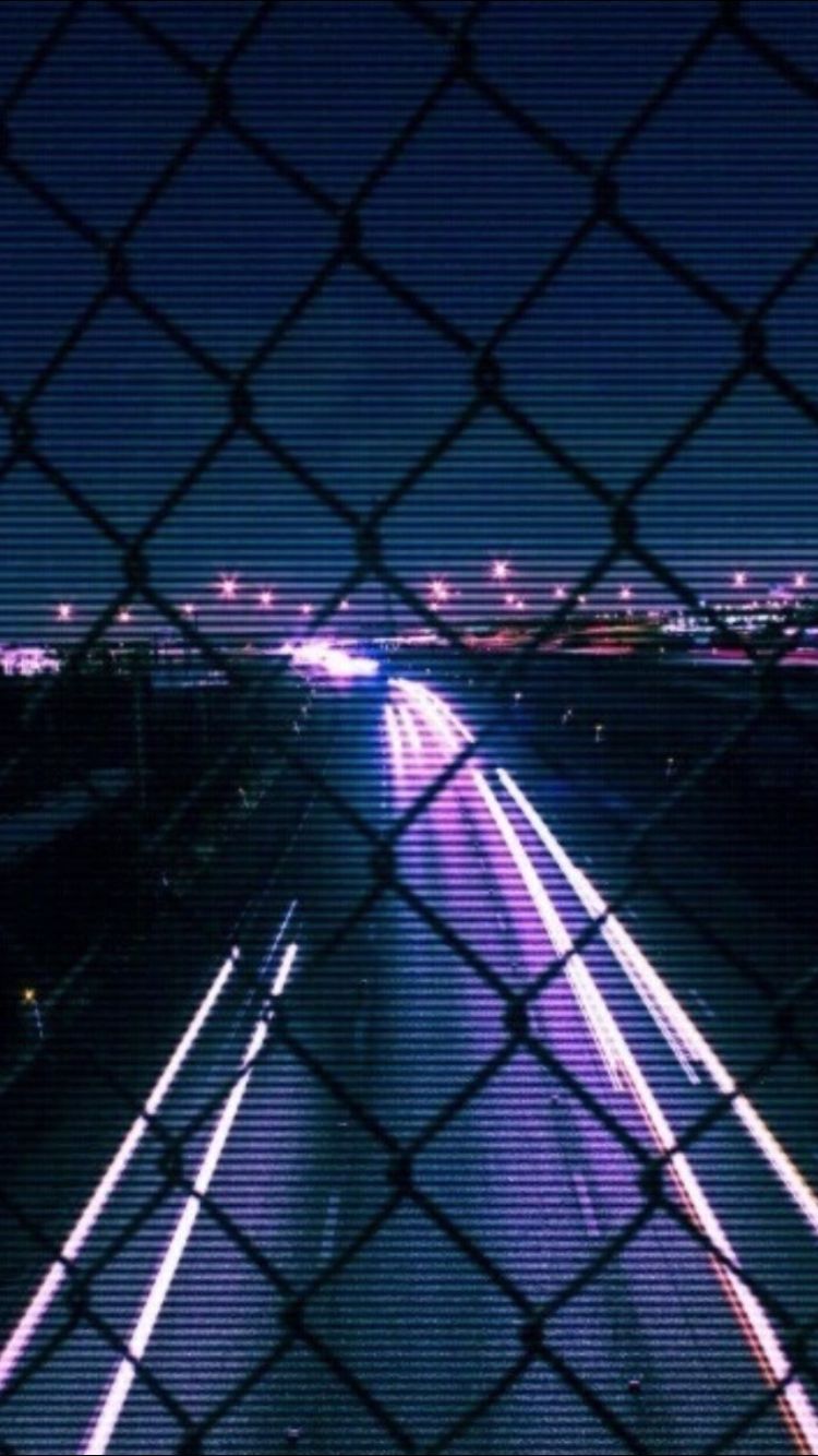 A chain link fence with a view of a highway at night - Dark purple