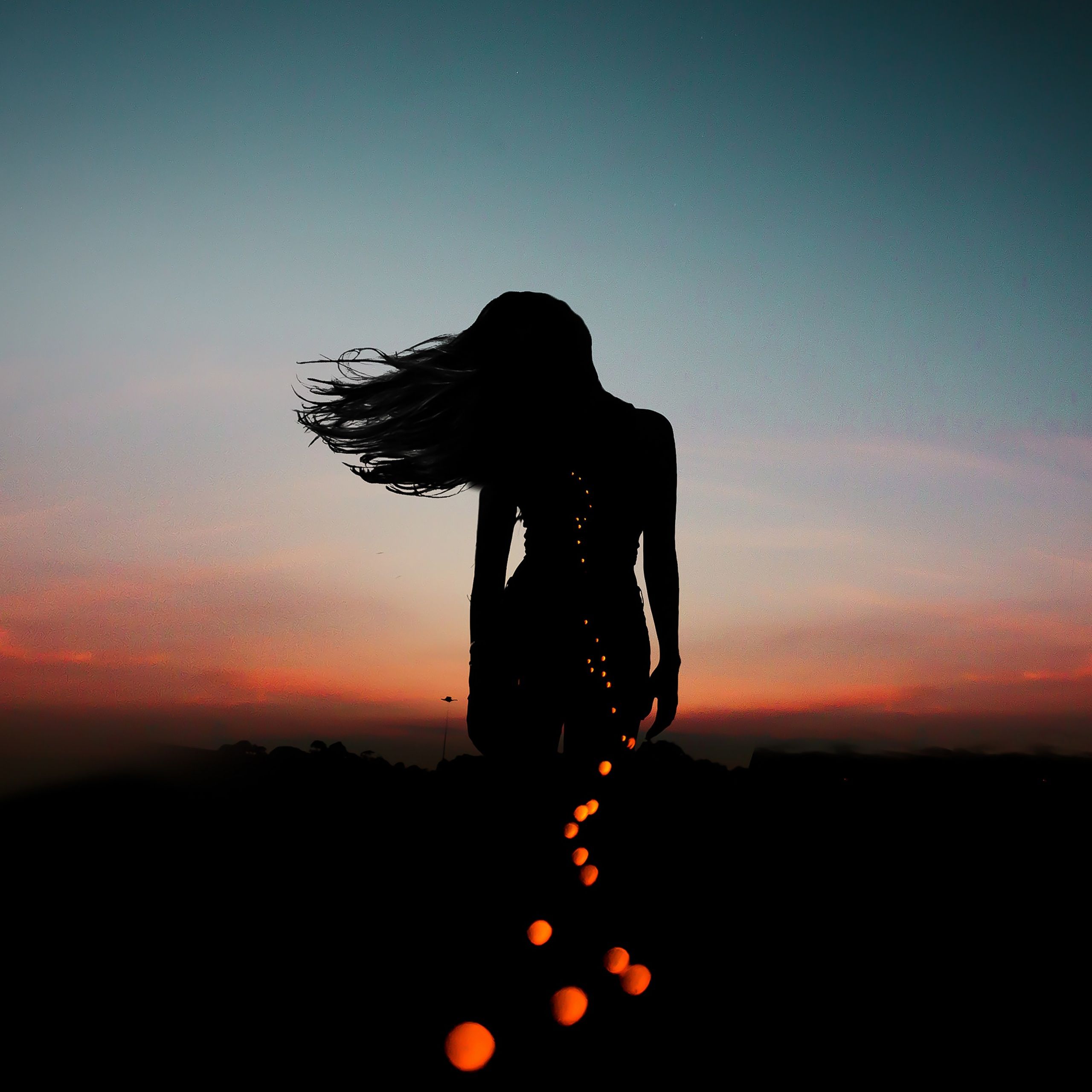 A woman with long hair stands in front of a sunset. - Sky