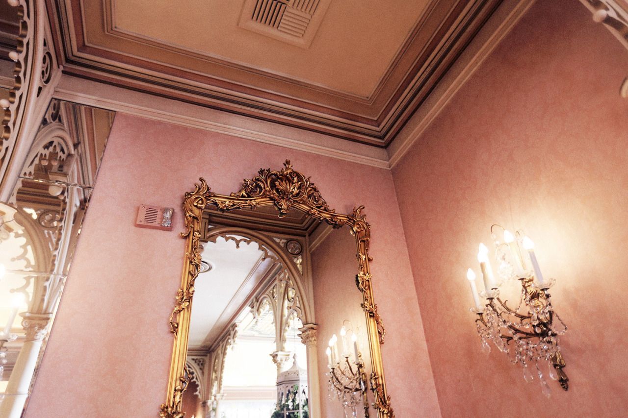 A pink wall with a gold framed mirror and a sconce. - Rose gold, blush