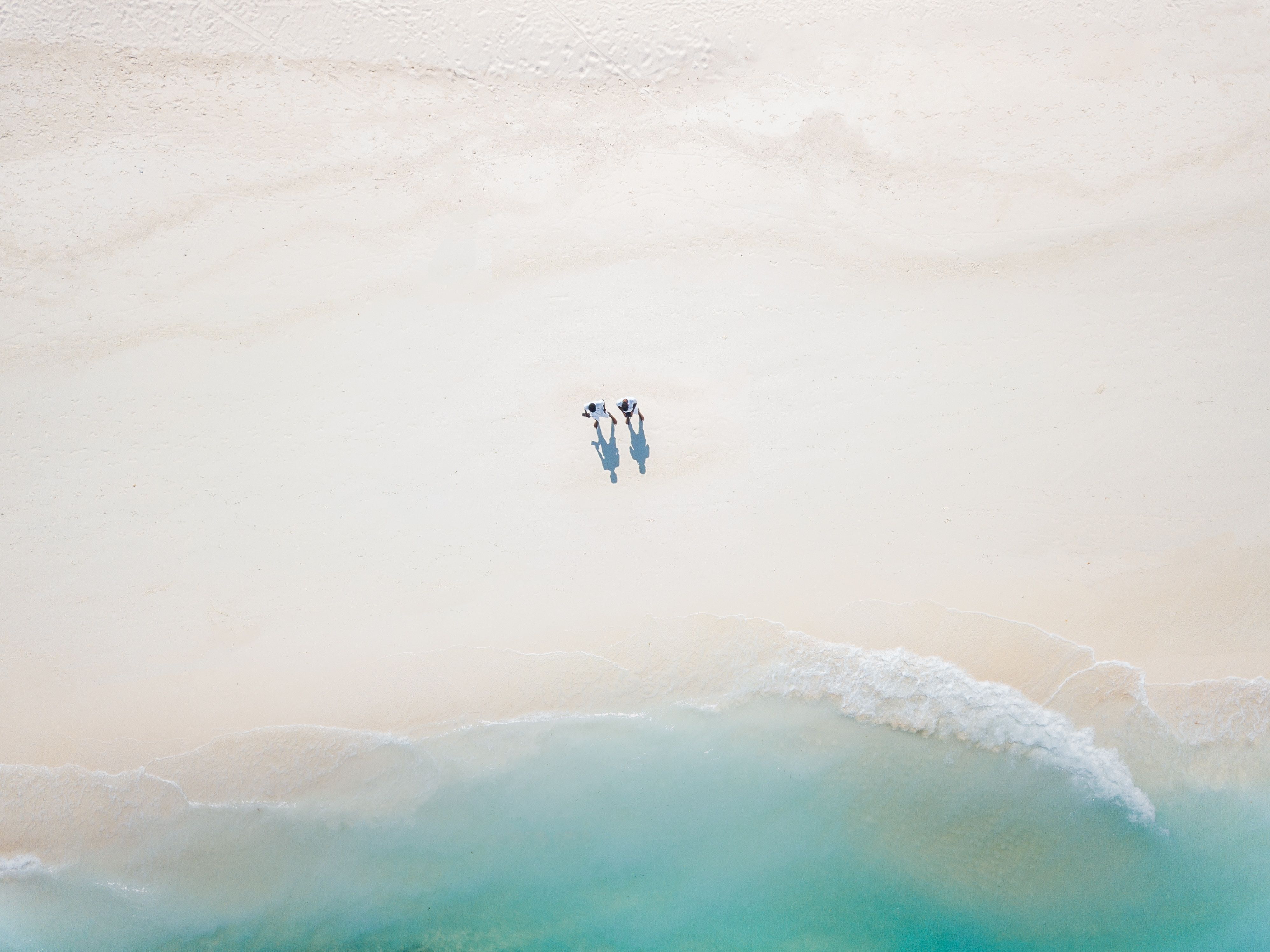 Aerial shot of three people standing on a white sand beach - Beach