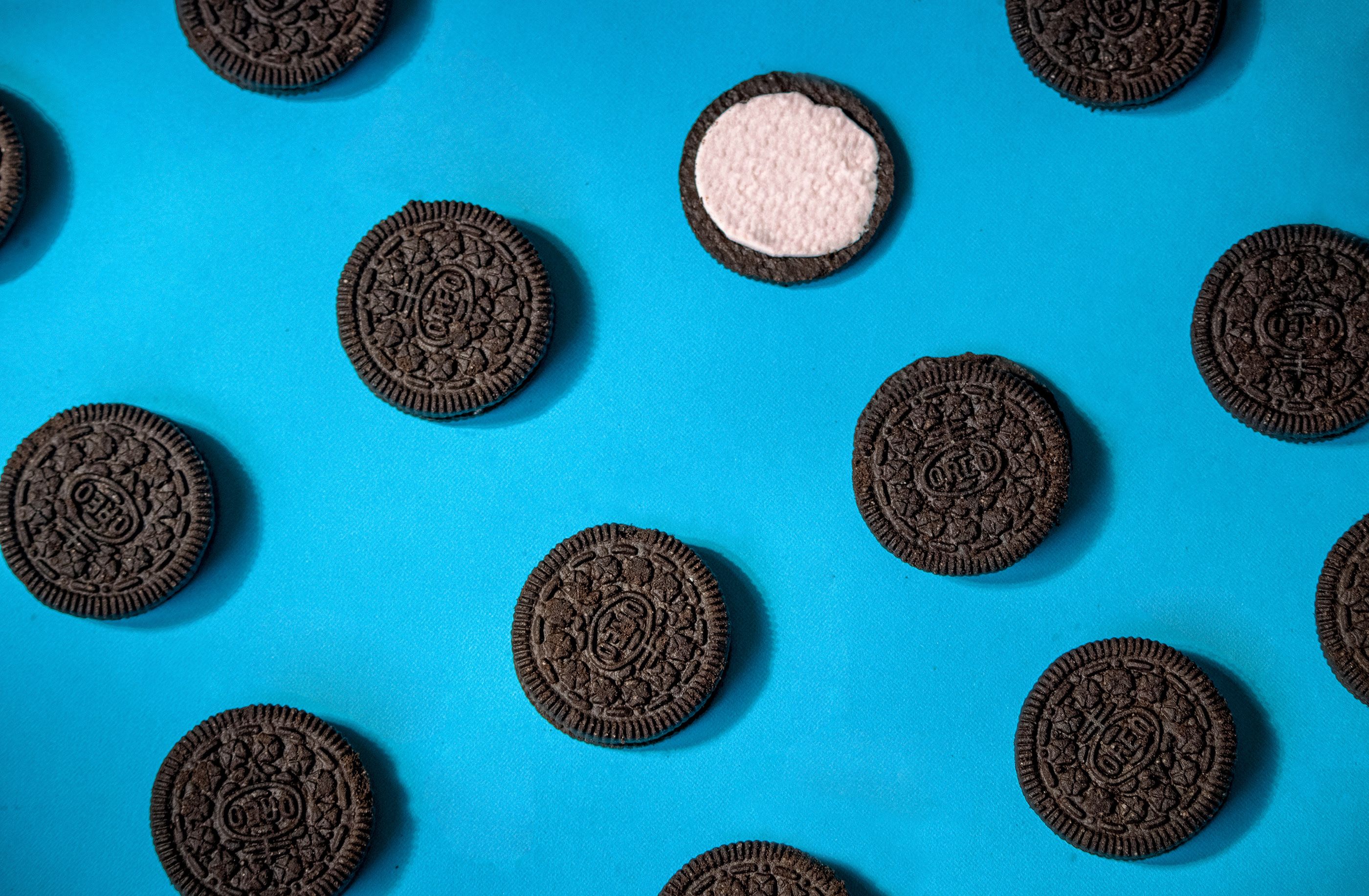 A pattern of chocolate sandwich cookies on a blue background, with one cookie missing the filling. - Oreo