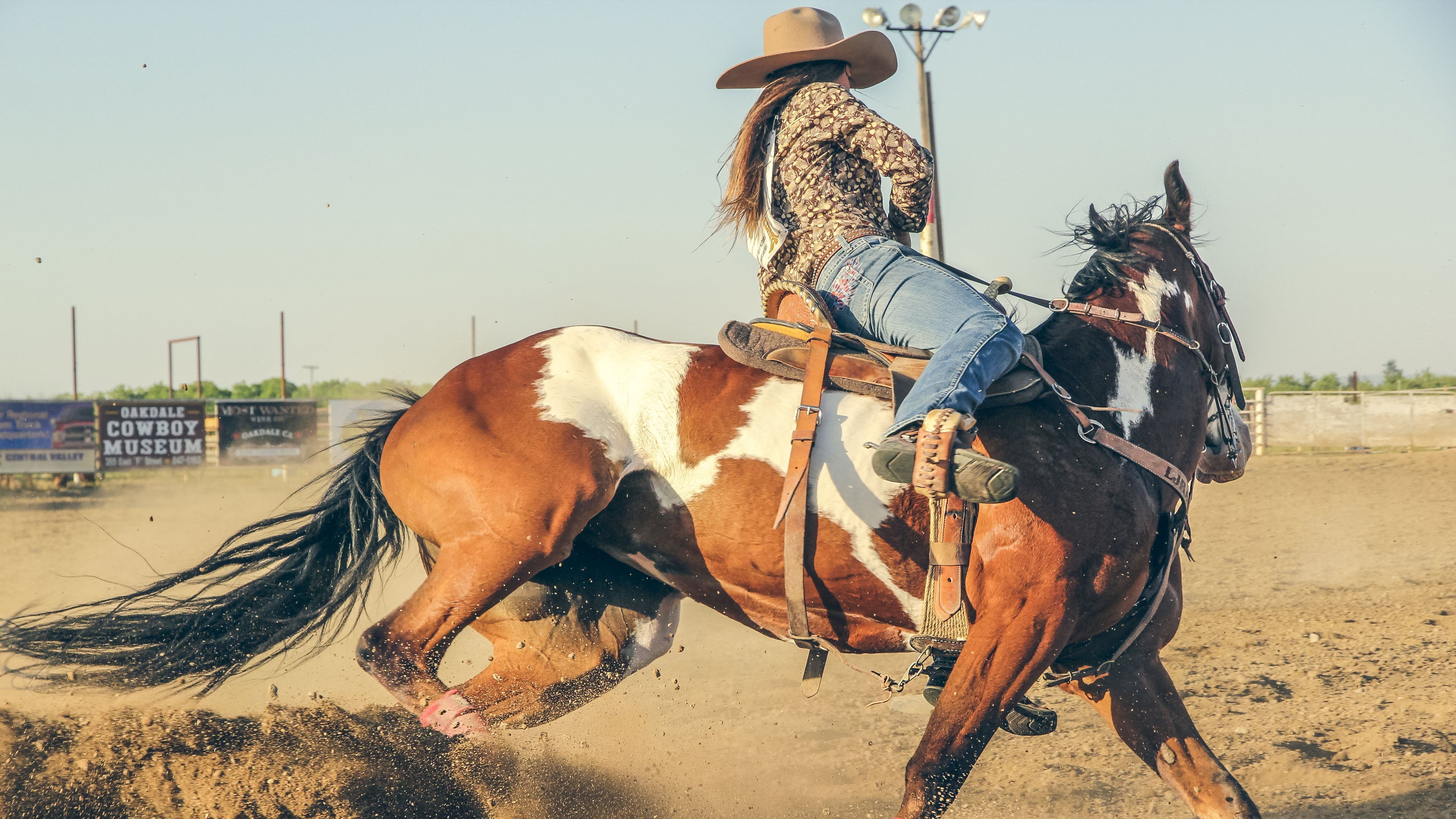 A woman in a cowboy hat rides a brown and white horse in a rodeo arena. - Cowgirl