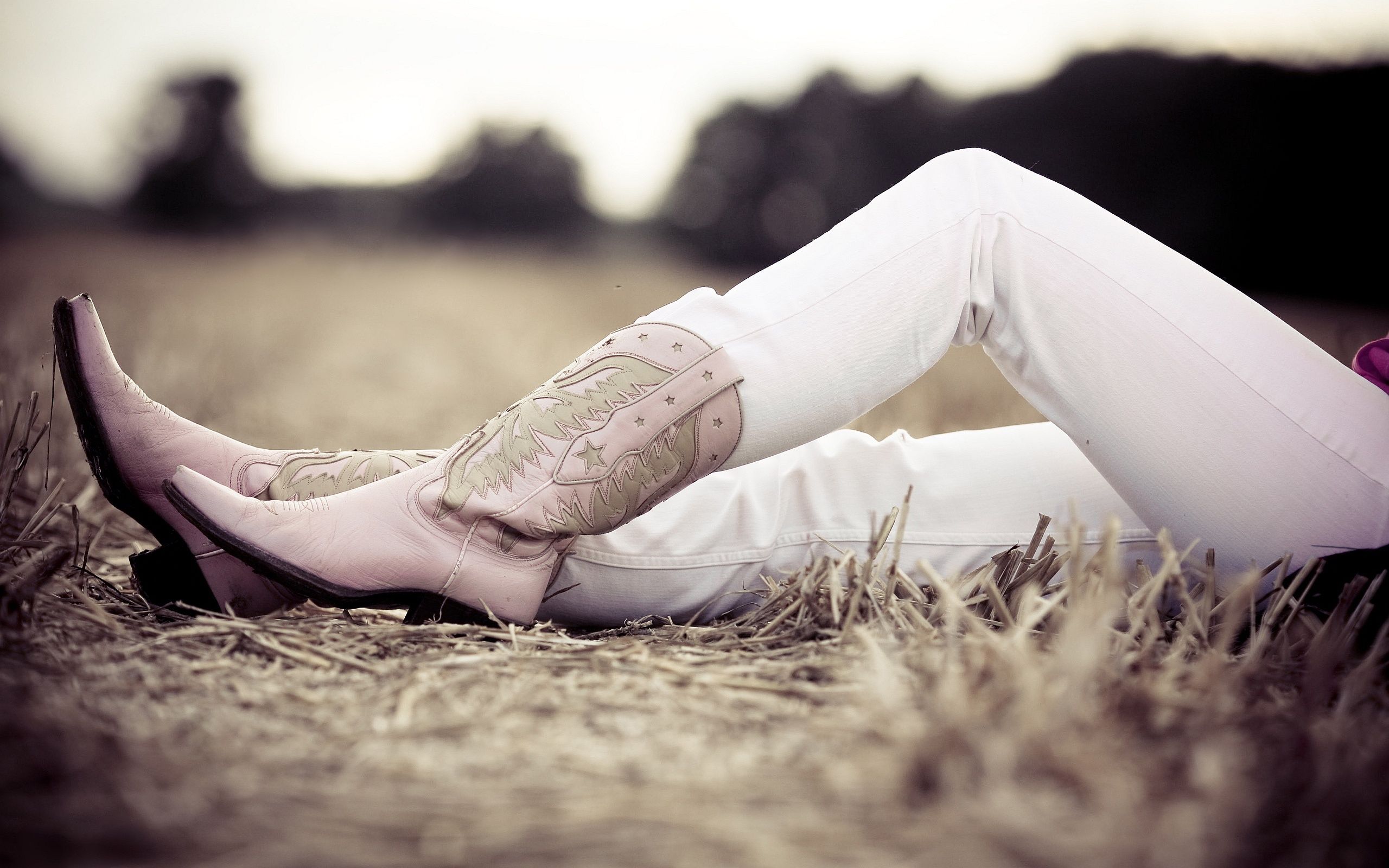 A woman laying in the grass with her boots on - Cowgirl