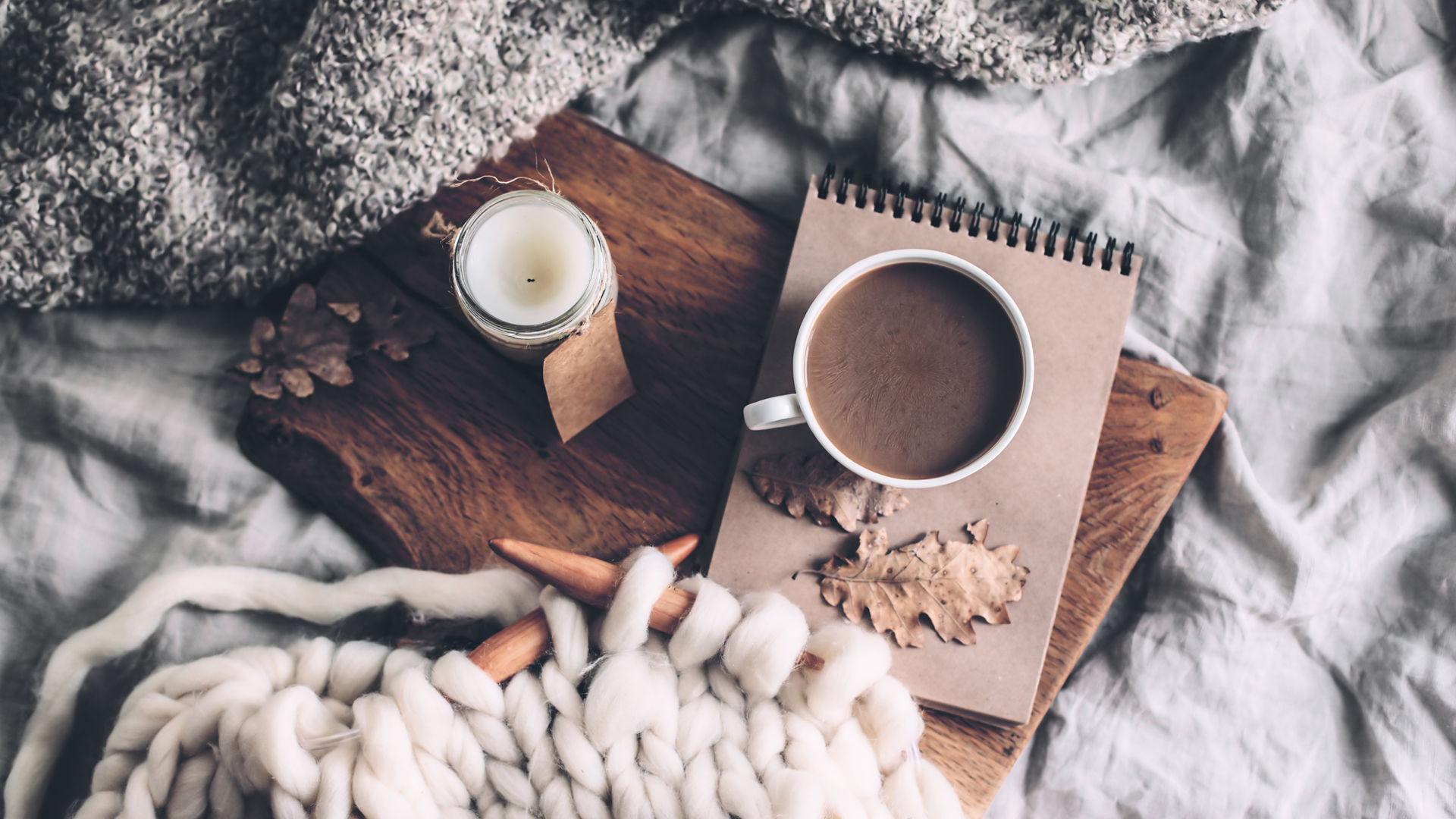 A cup of coffee, a book, a candle and a blanket on a bed. - Cozy