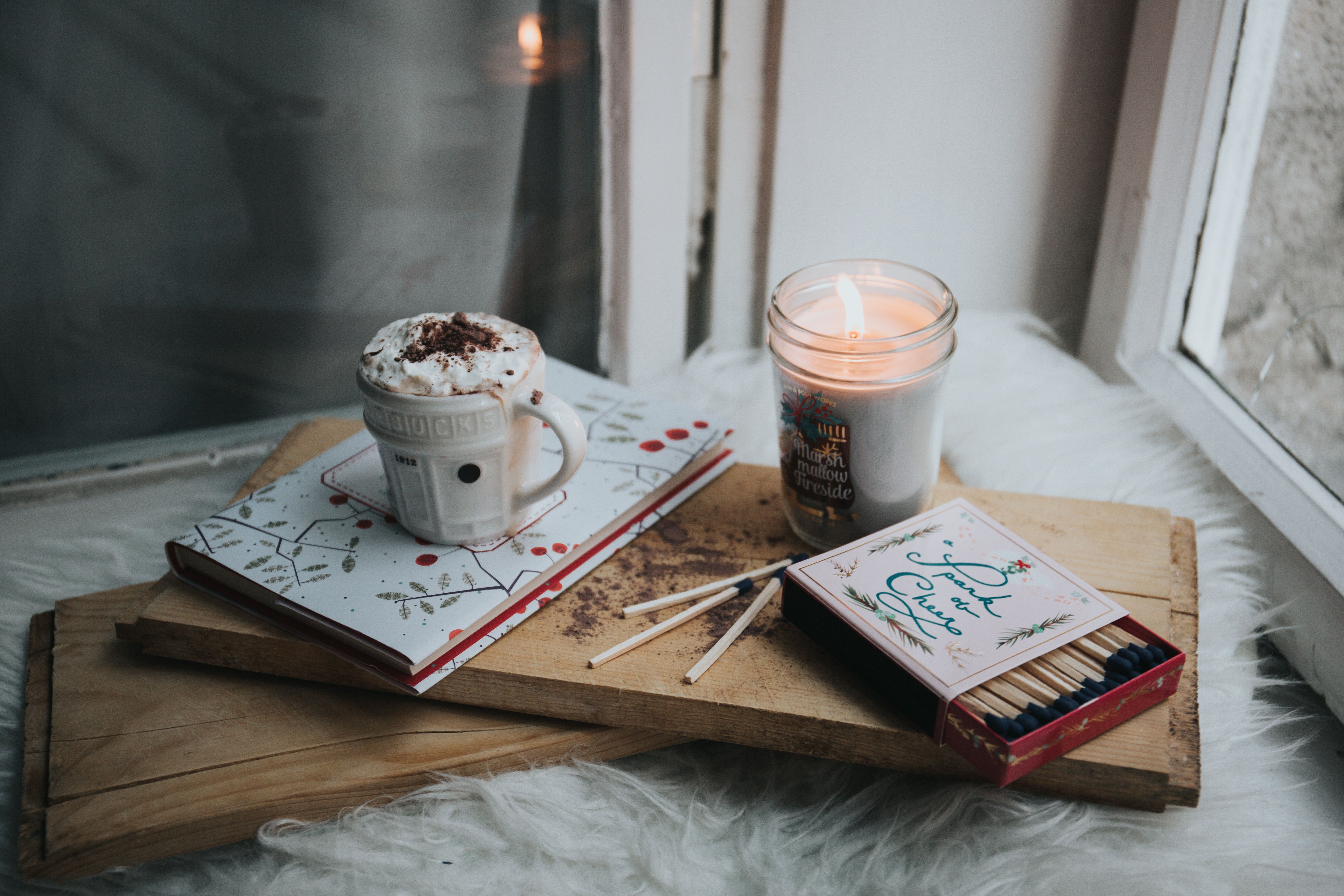 A candle, book and matches on top of some wood - Cozy