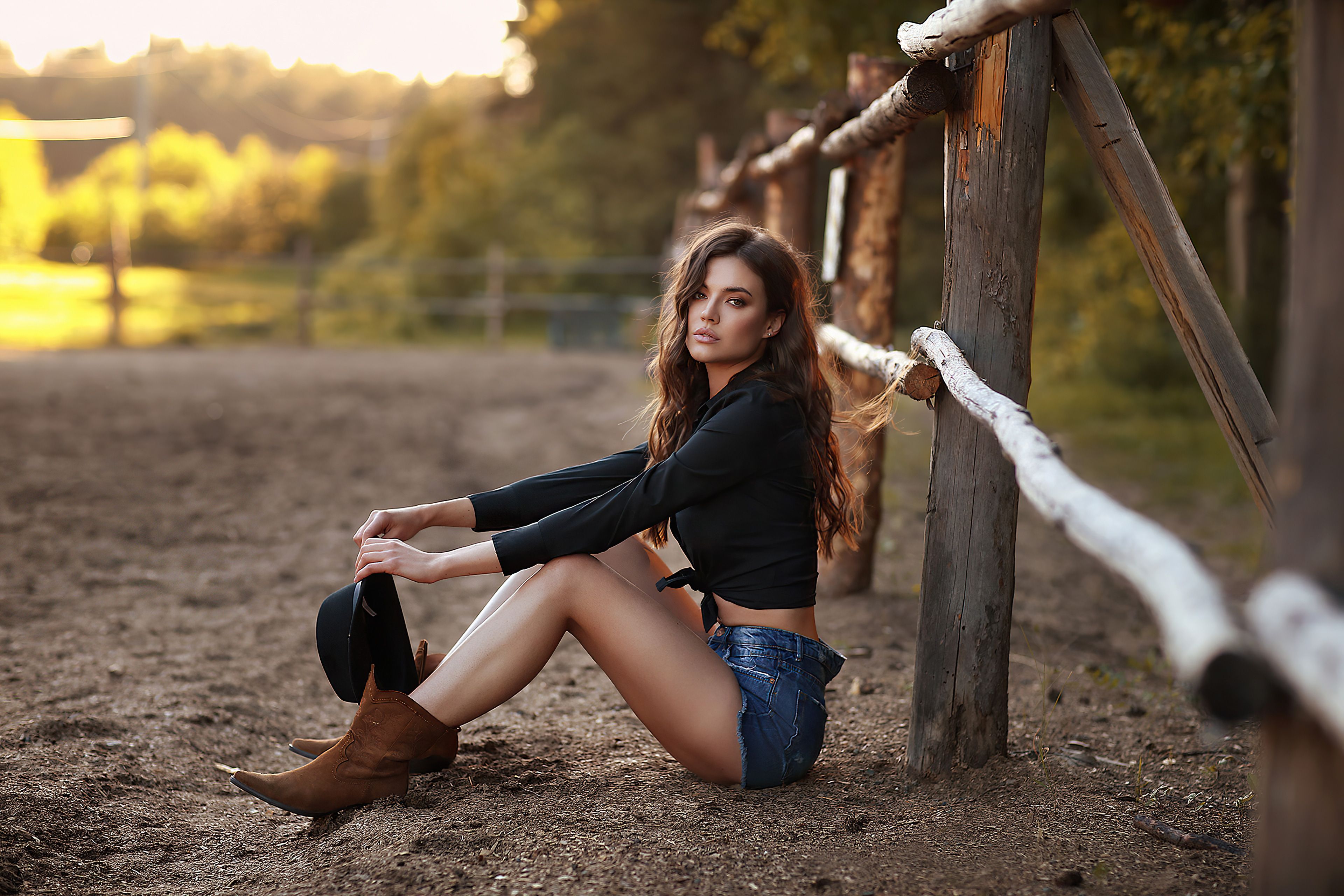 A woman sitting on the ground near a fence - Cowgirl