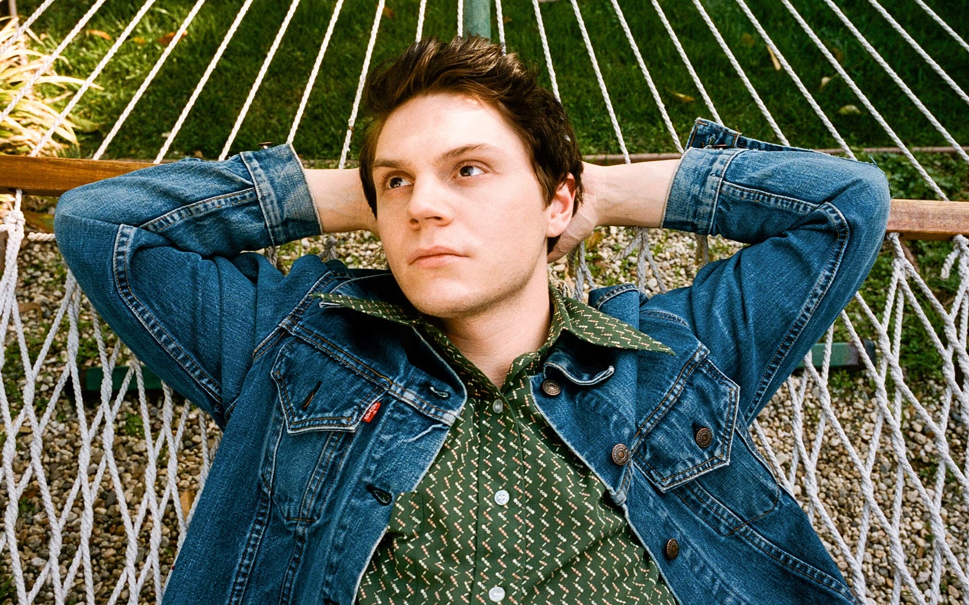 A man in blue jeans and shirt is laying on hammock - Evan Peters