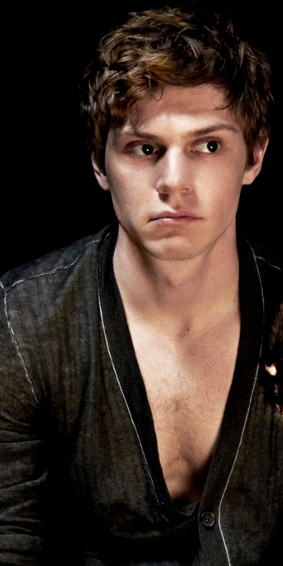 Evan Peters as Tate in American Horror Story: Hotel. Tate is a young man with brown hair and a brown button up with the top two buttons undone. He is looking off to the side with a serious expression on his face. - Evan Peters