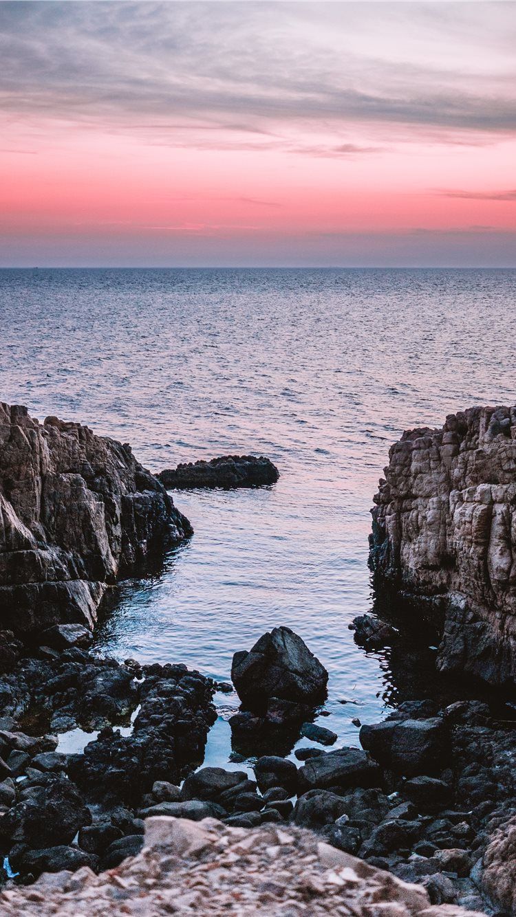 A rocky beach at sunset with the sky in shades of pink and purple. - Rocks