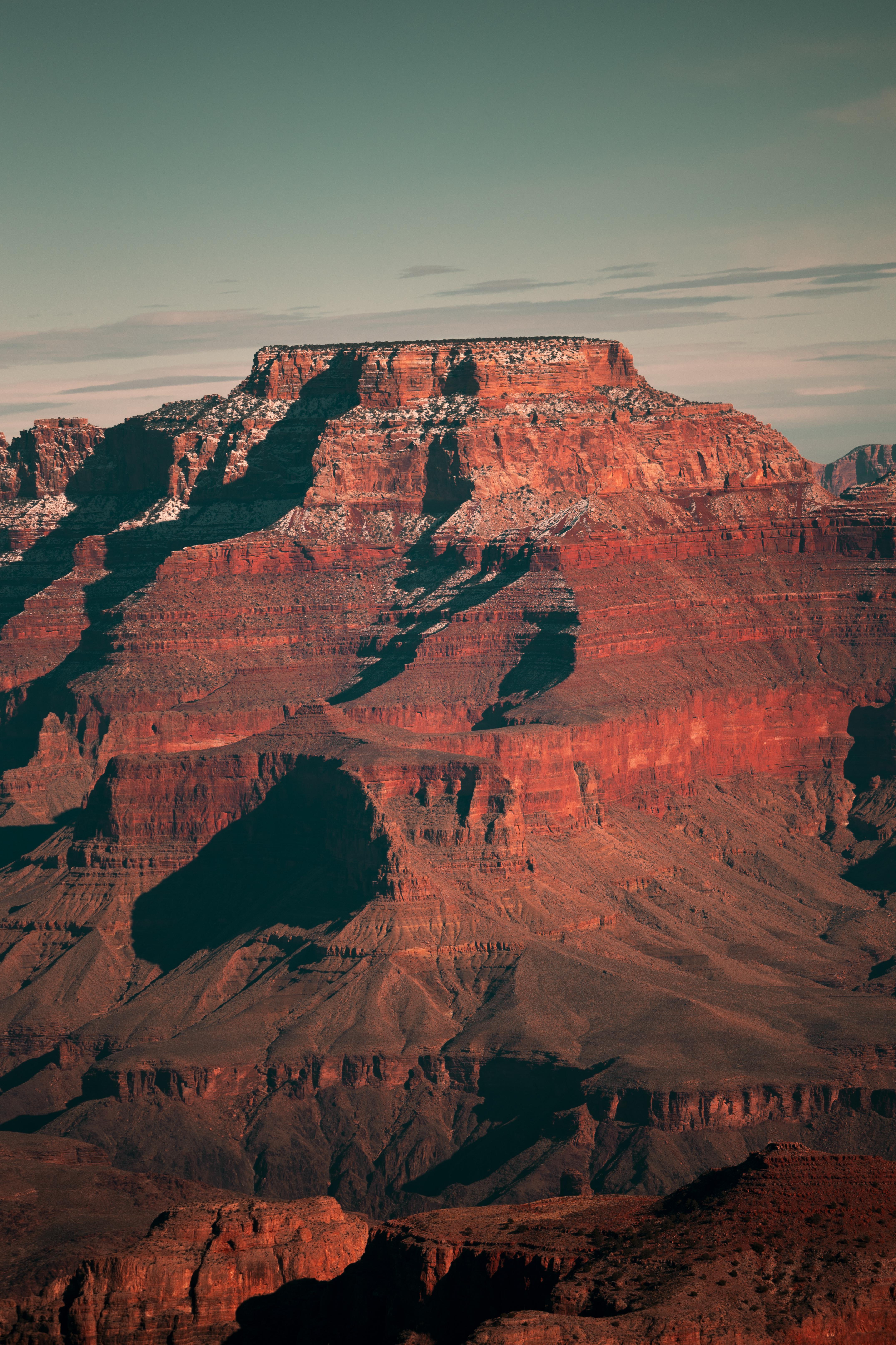 A snow-capped mountain peak looms in the distance, casting a long shadow over the red rock below. - Rocks