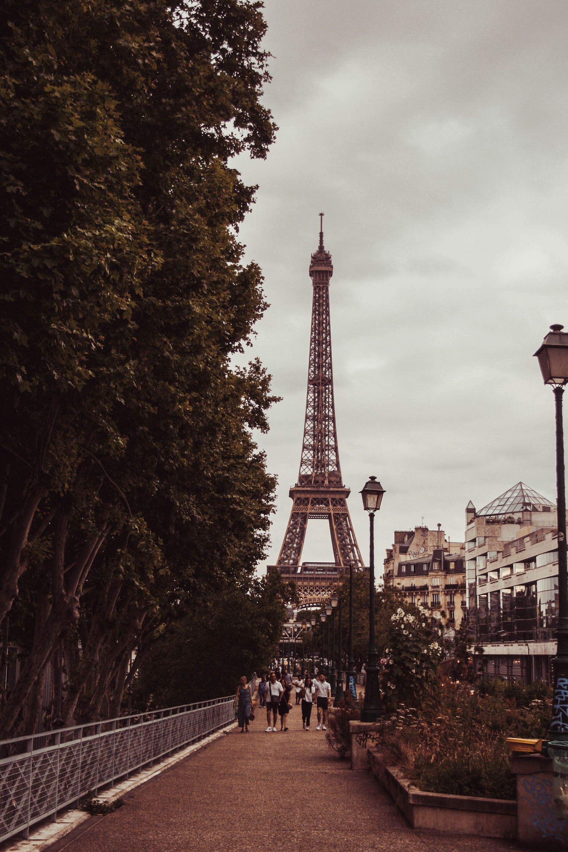 A walkway leading to the Eiffel Tower with a grey sky overhead. - Paris