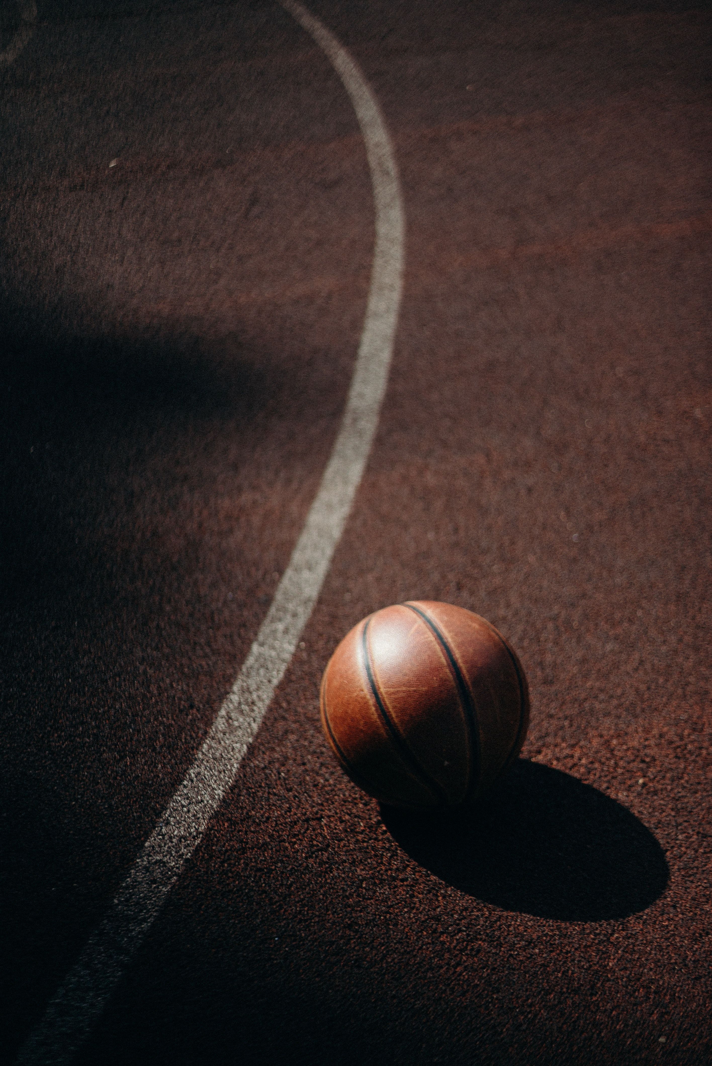 A basketball sitting on the floor of an empty court - Basketball