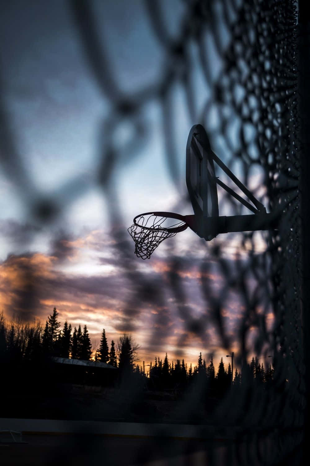 A basketball hoop is silhouetted against a cloudy sky - Basketball