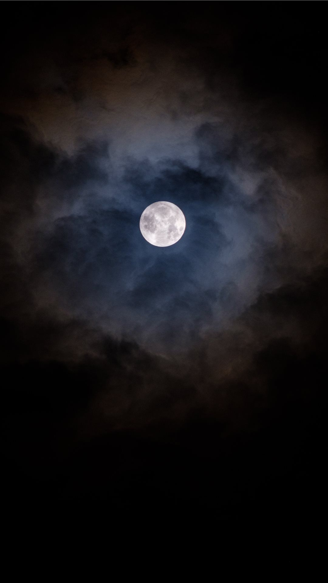 The full moon in the sky, partially obscured by clouds. - Moon