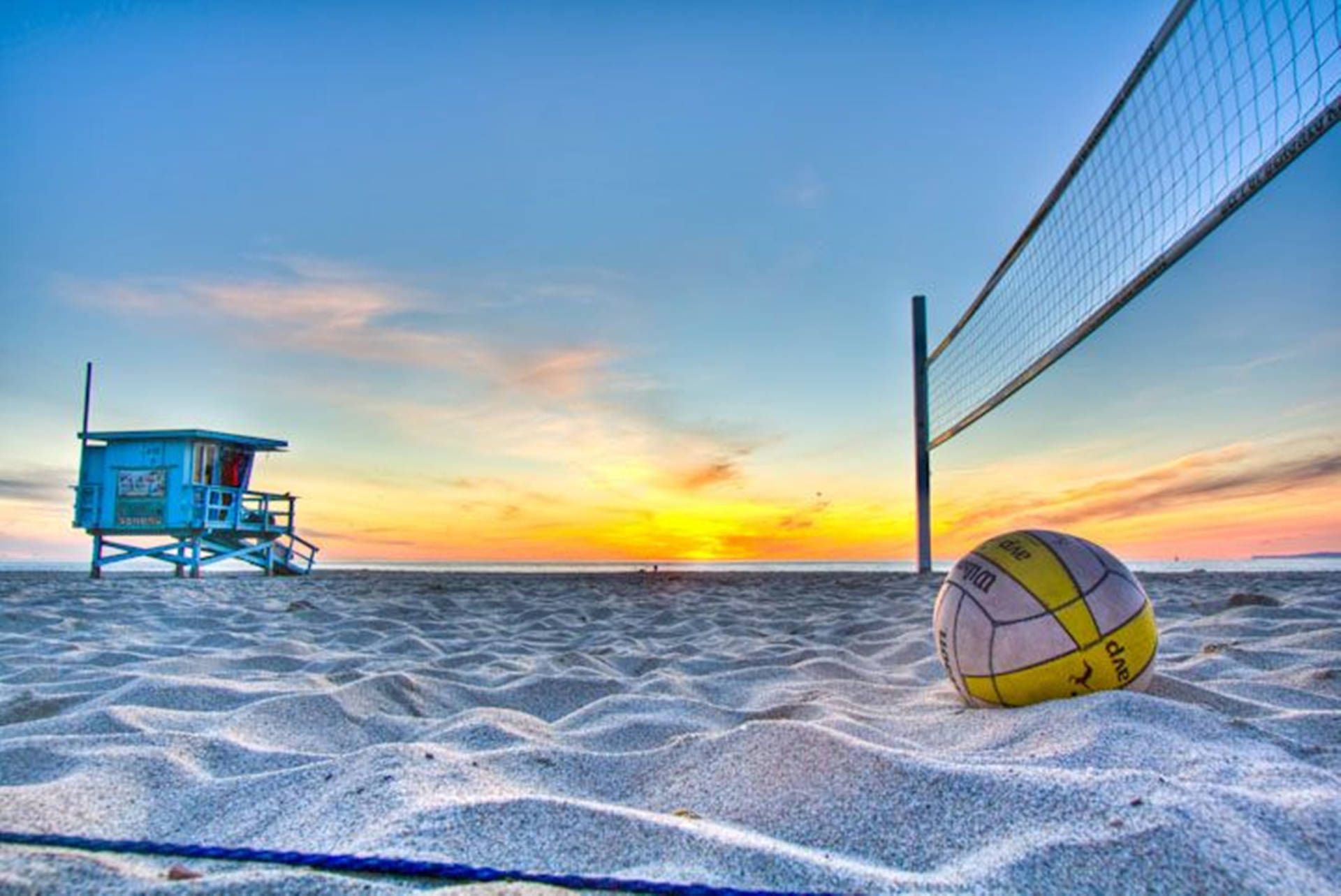 A volleyball sitting on the sand at sunset - Volleyball