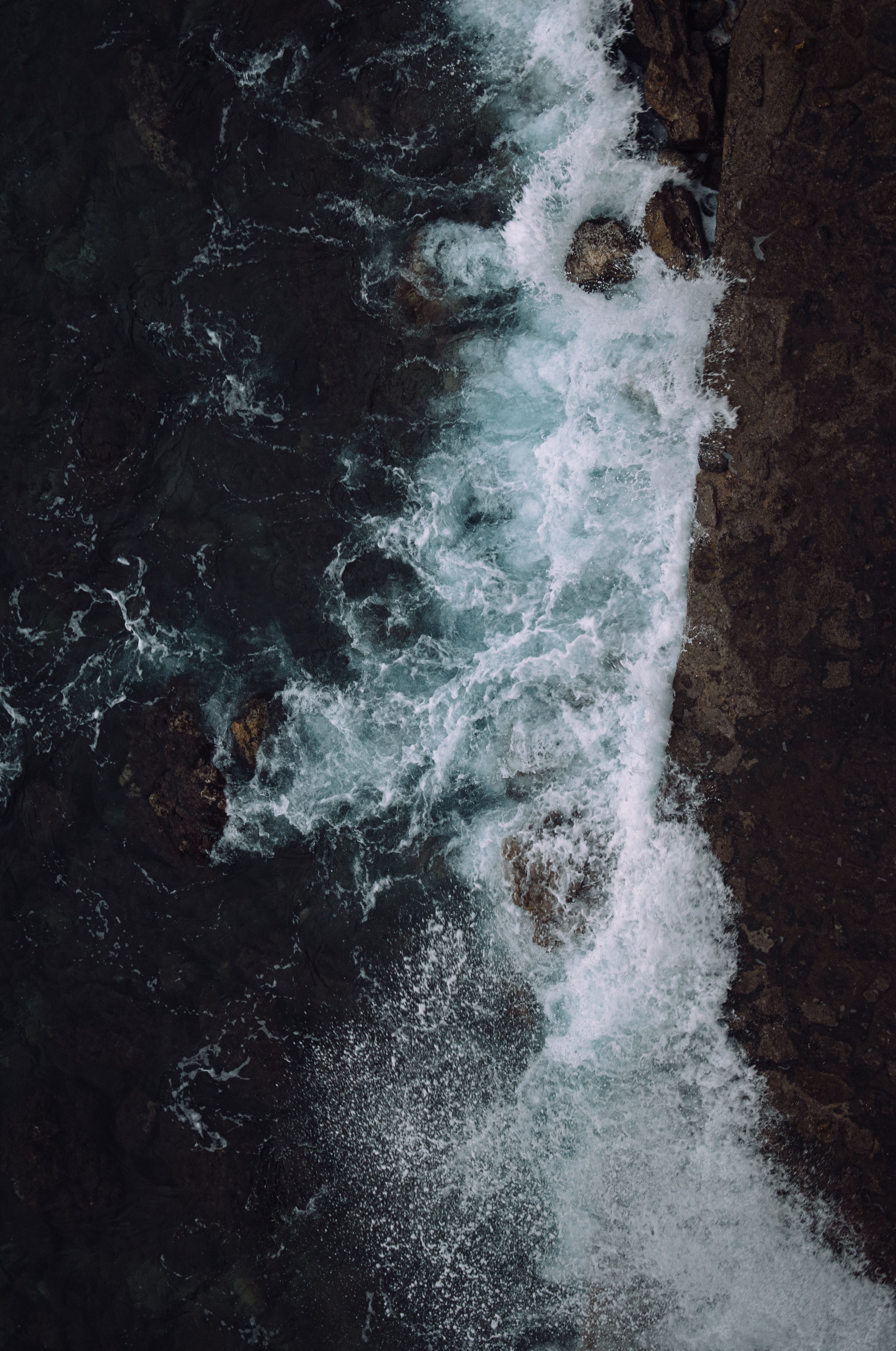 Aerial view of waves crashing against a rocky cliff - Wave