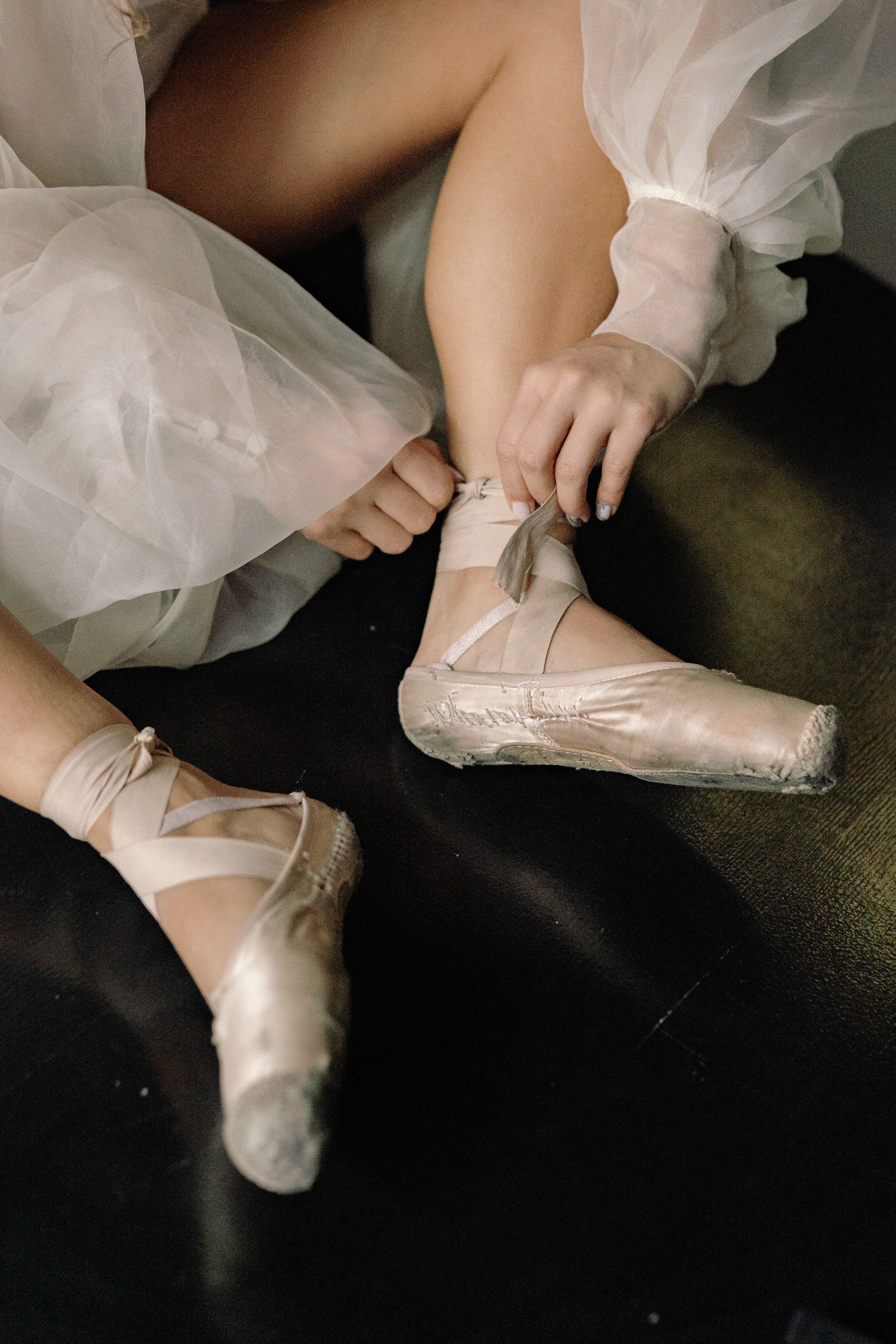 A ballerina sits on the floor and ties her white pointe shoes. - Ballet