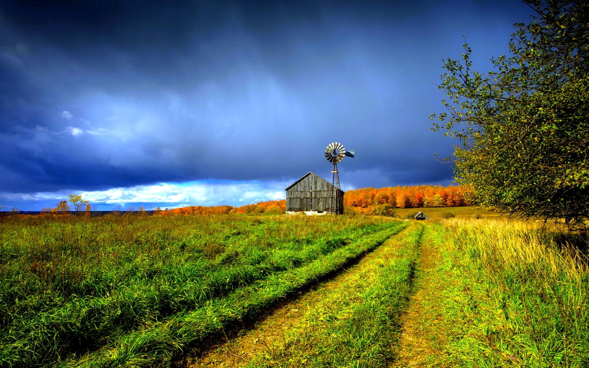 A country road with a barn and windmill in the distance. - Farm