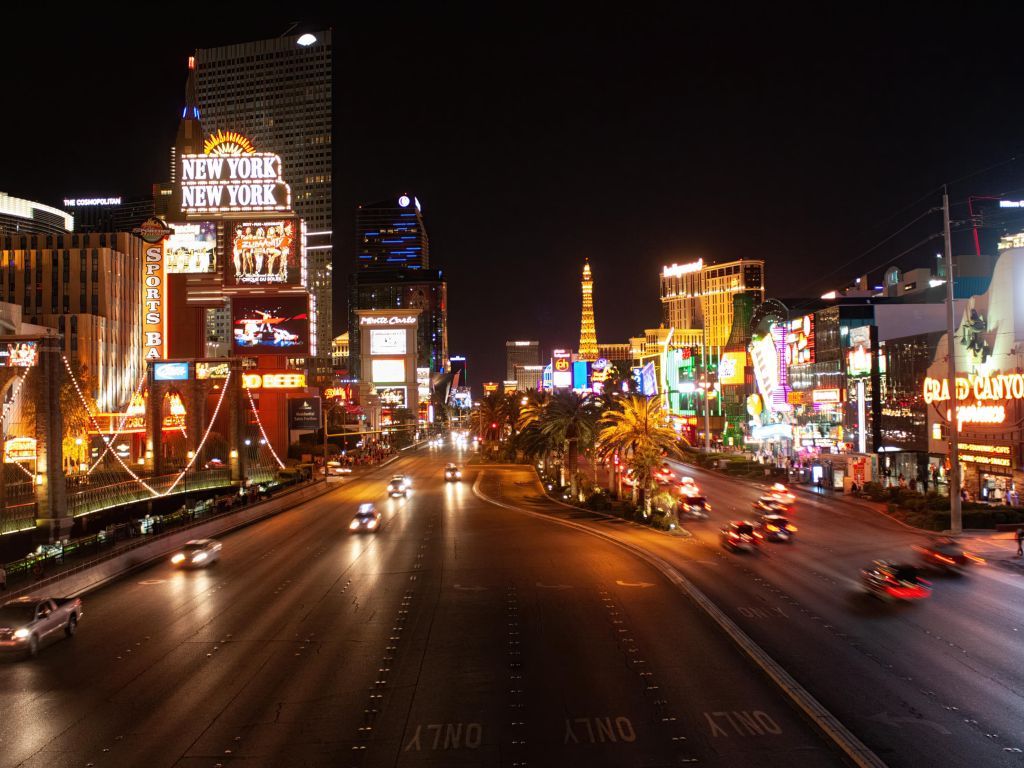 A city street at night with neon lights and cars - Las Vegas