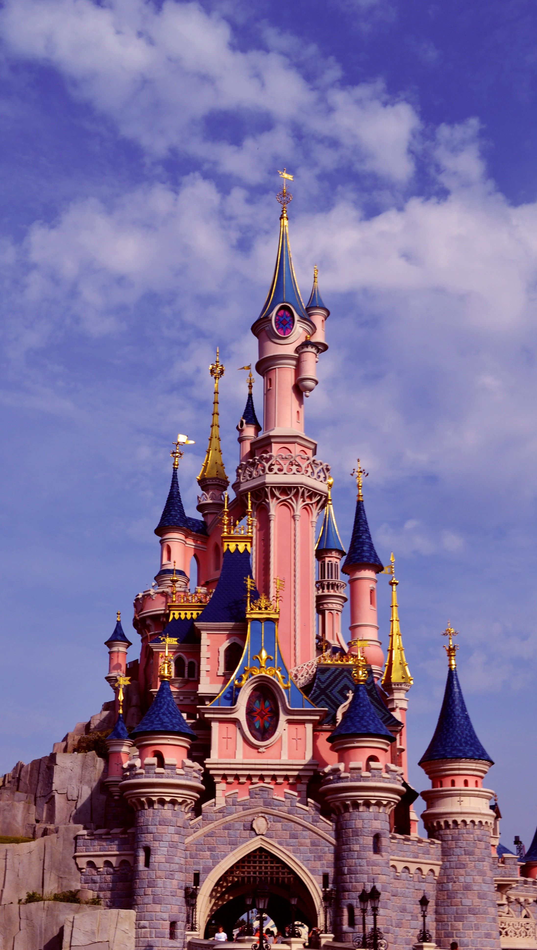 The castle is pink and blue with a large tower - Disneyland