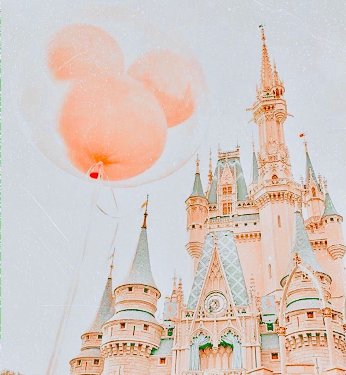 A pink balloon in the shape of Mickey Mouse's head floats in front of the Disney castle. - Disneyland