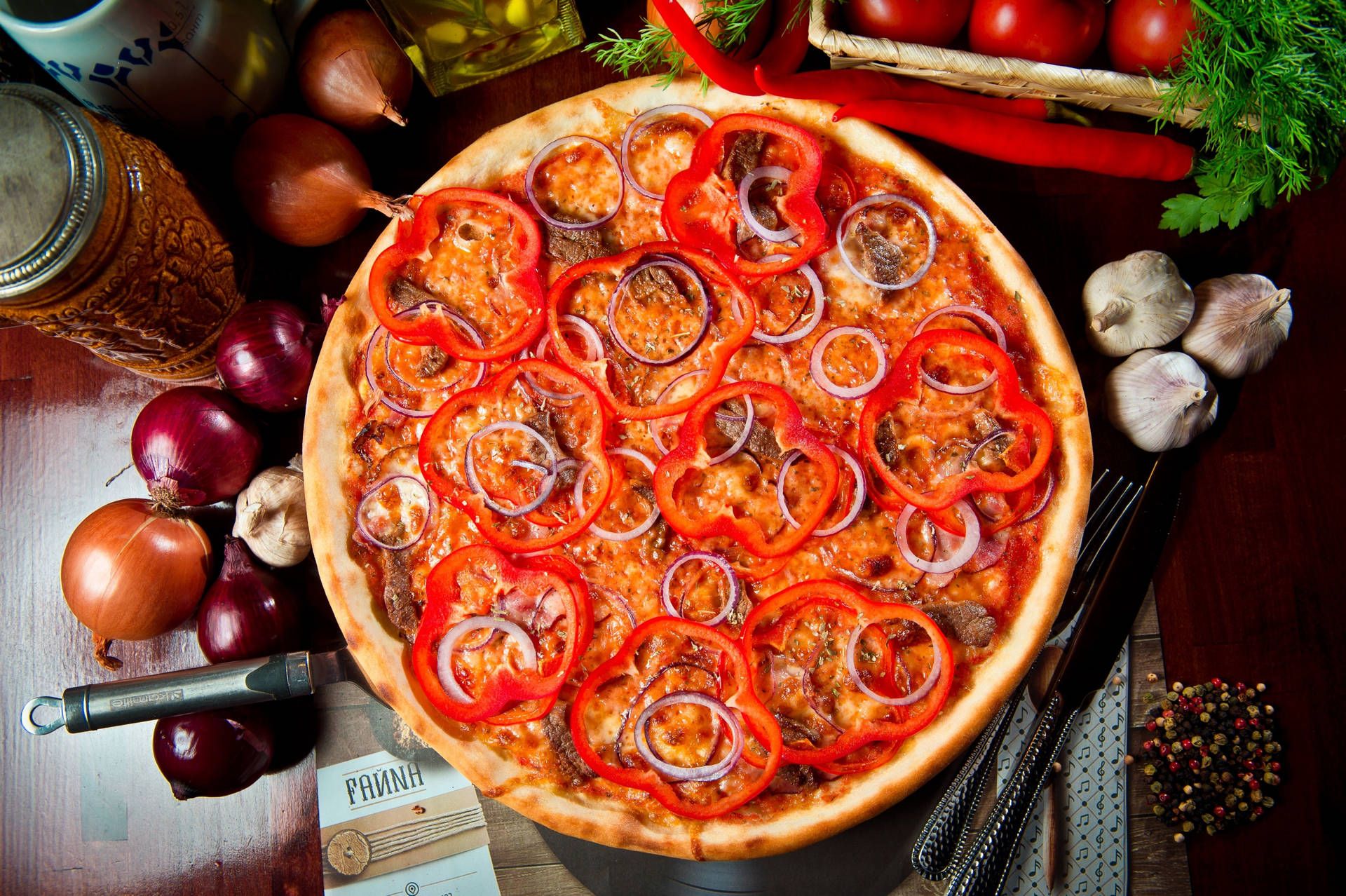 A pizza with tomatoes, onions, and peppers on a wooden table. - Pizza