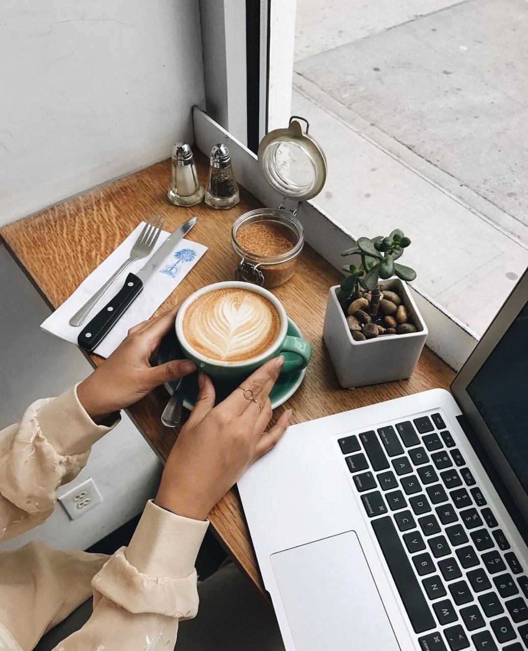 A woman holding a cup of coffee in front of a laptop. - Coffee