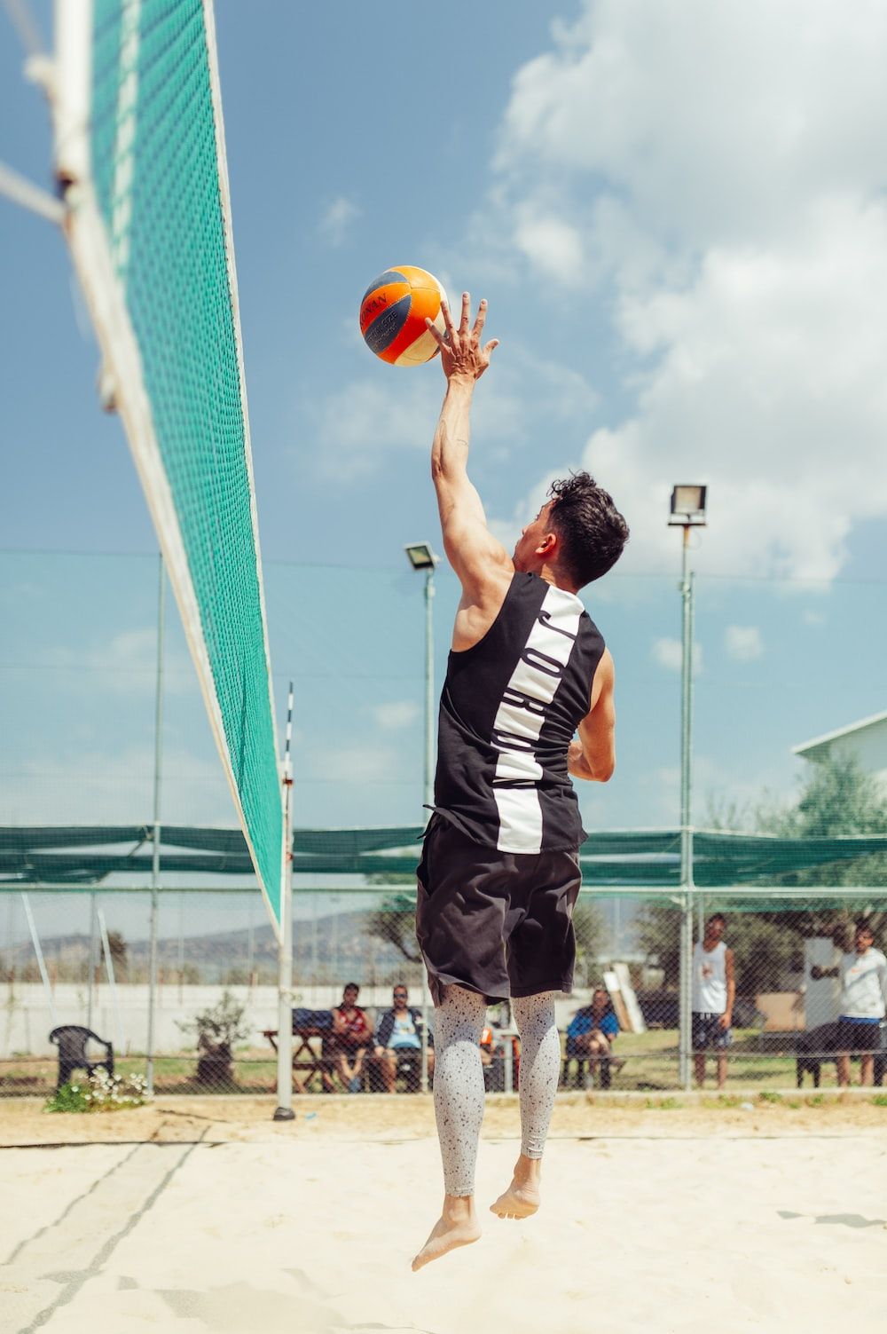 A man in a black shirt jumps to hit a volleyball over the net. - Volleyball