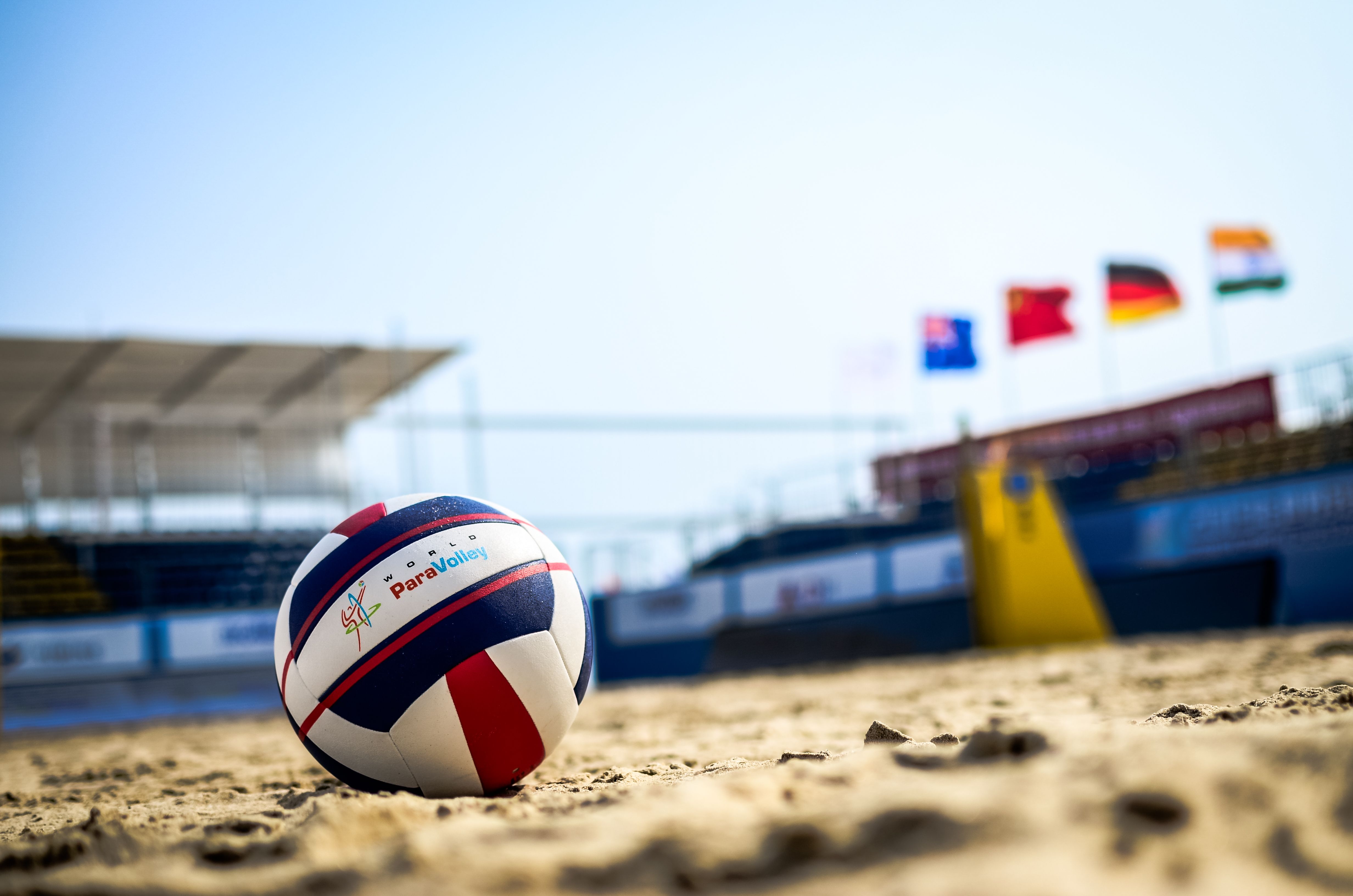 A volleyball on the sand with flags in the background. - Volleyball