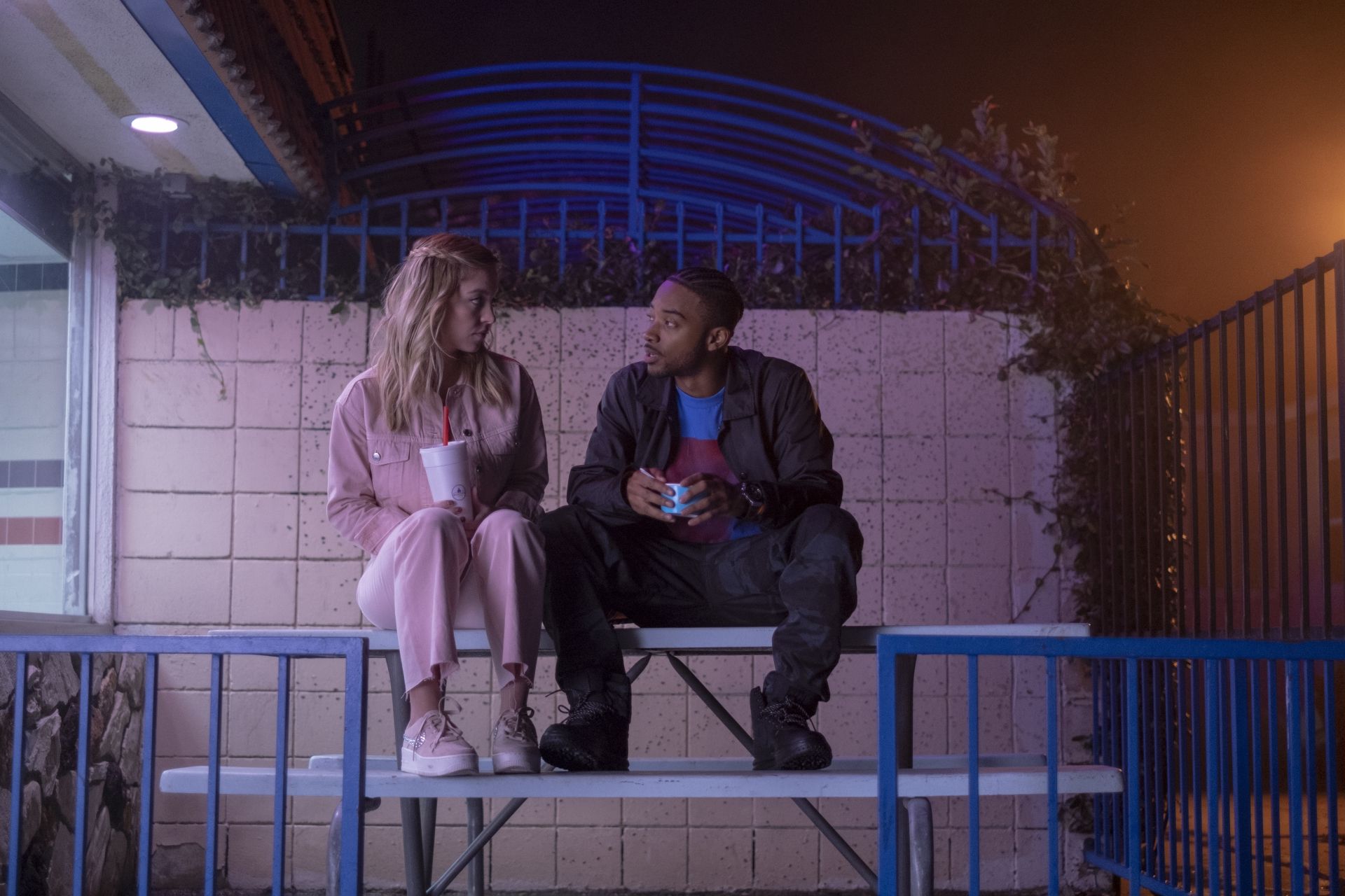 A young woman and man sit on a bench in a parking lot - Euphoria