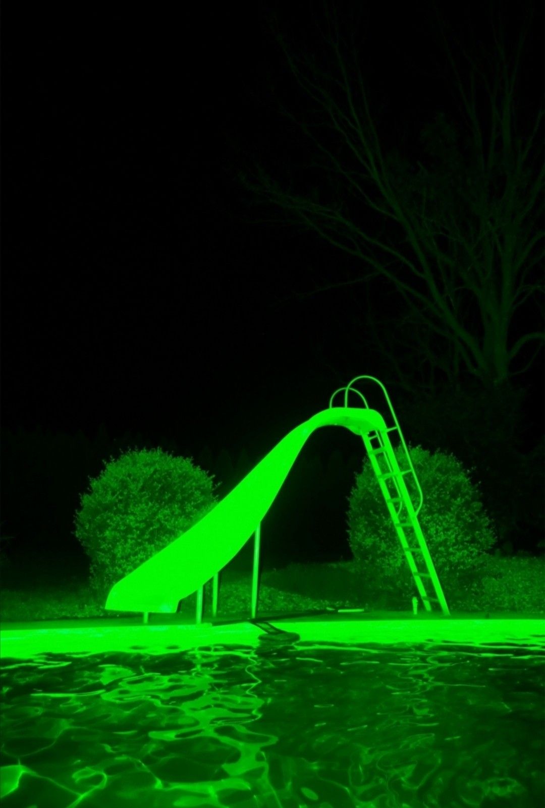 A pool slide glows green in the dark. - Neon green