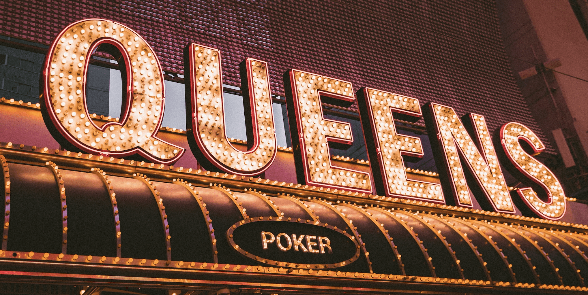 A sign for the Queen's Poker room is lit up at night. - Neon orange