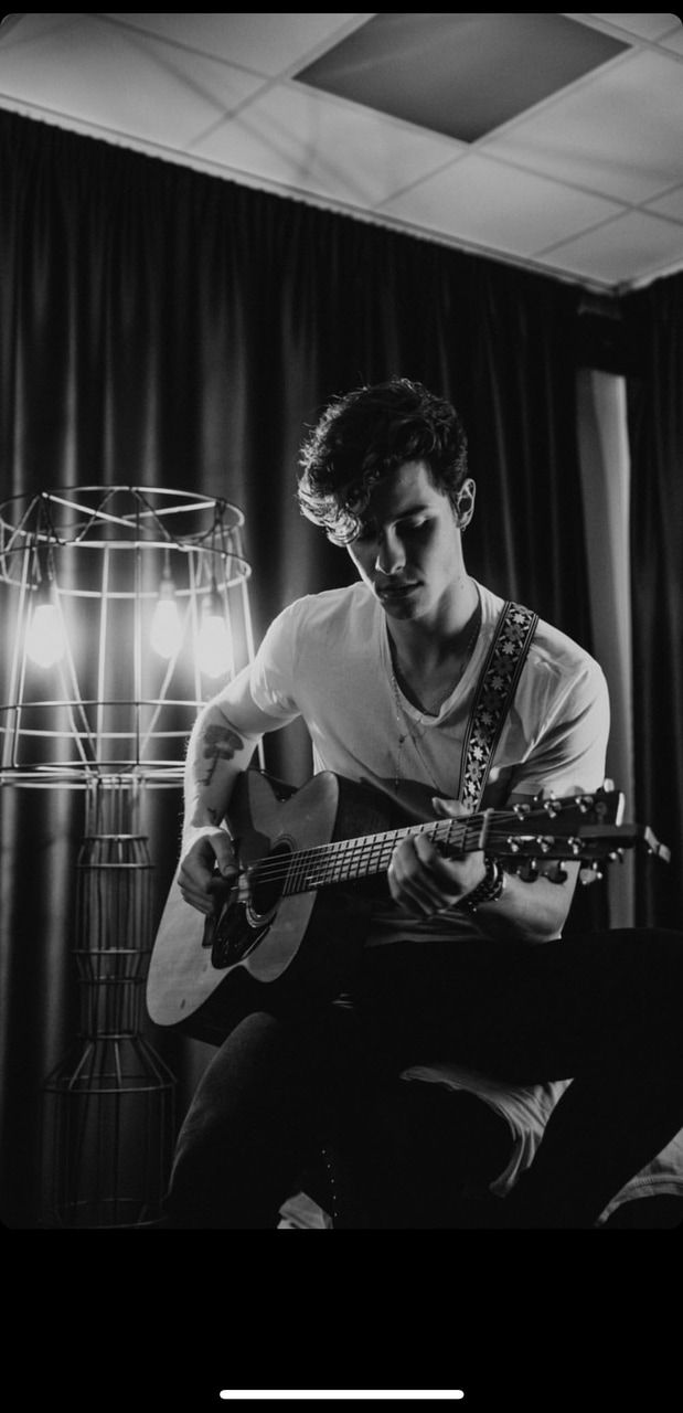 A man sitting on the floor playing guitar - Shawn Mendes