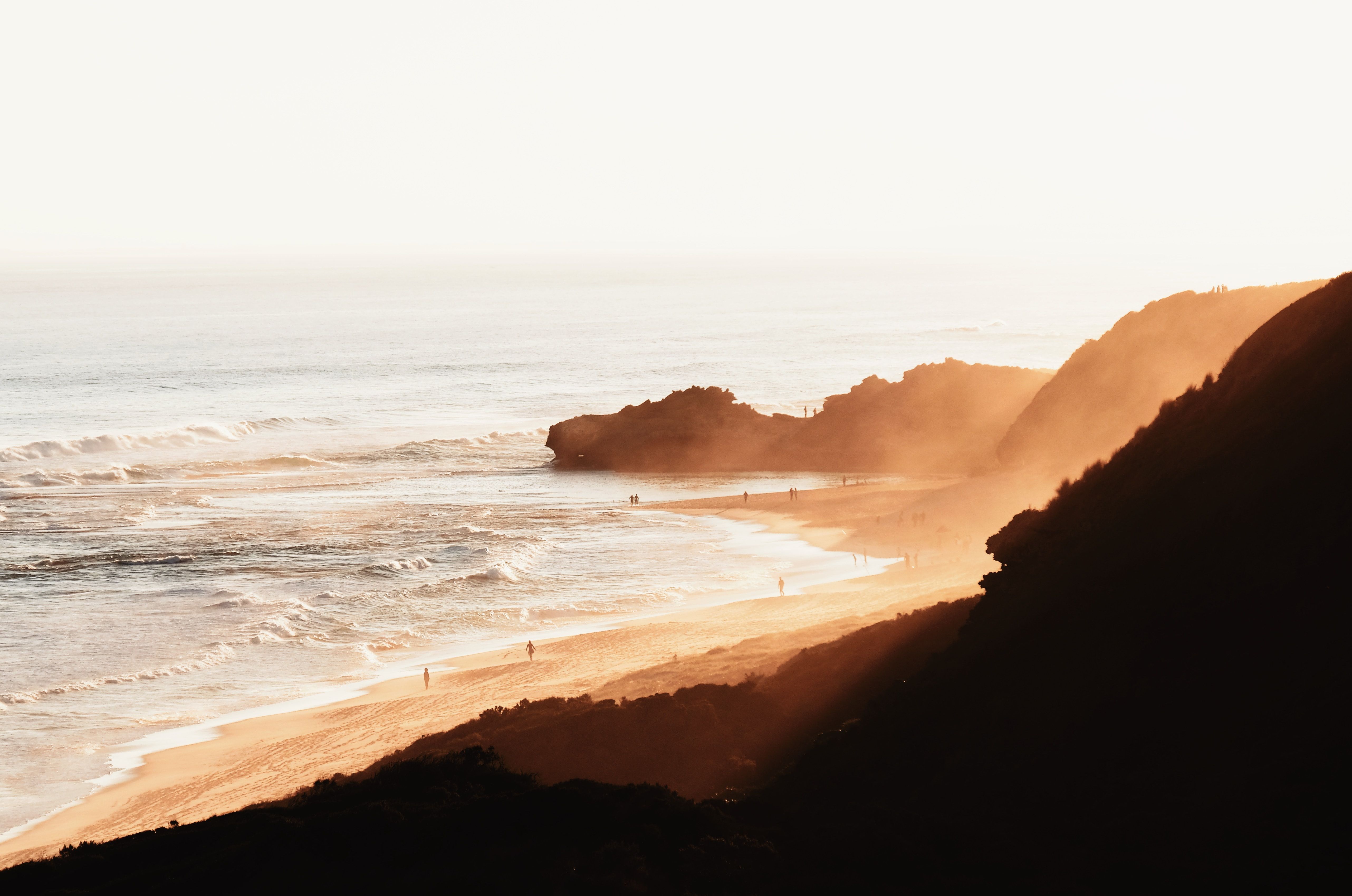 A beach with a hillside and the sun setting - MacBook, coast