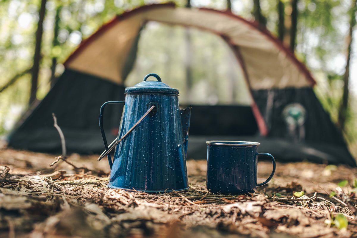 A blue coffee pot and cup sitting next to an open tent - Camping